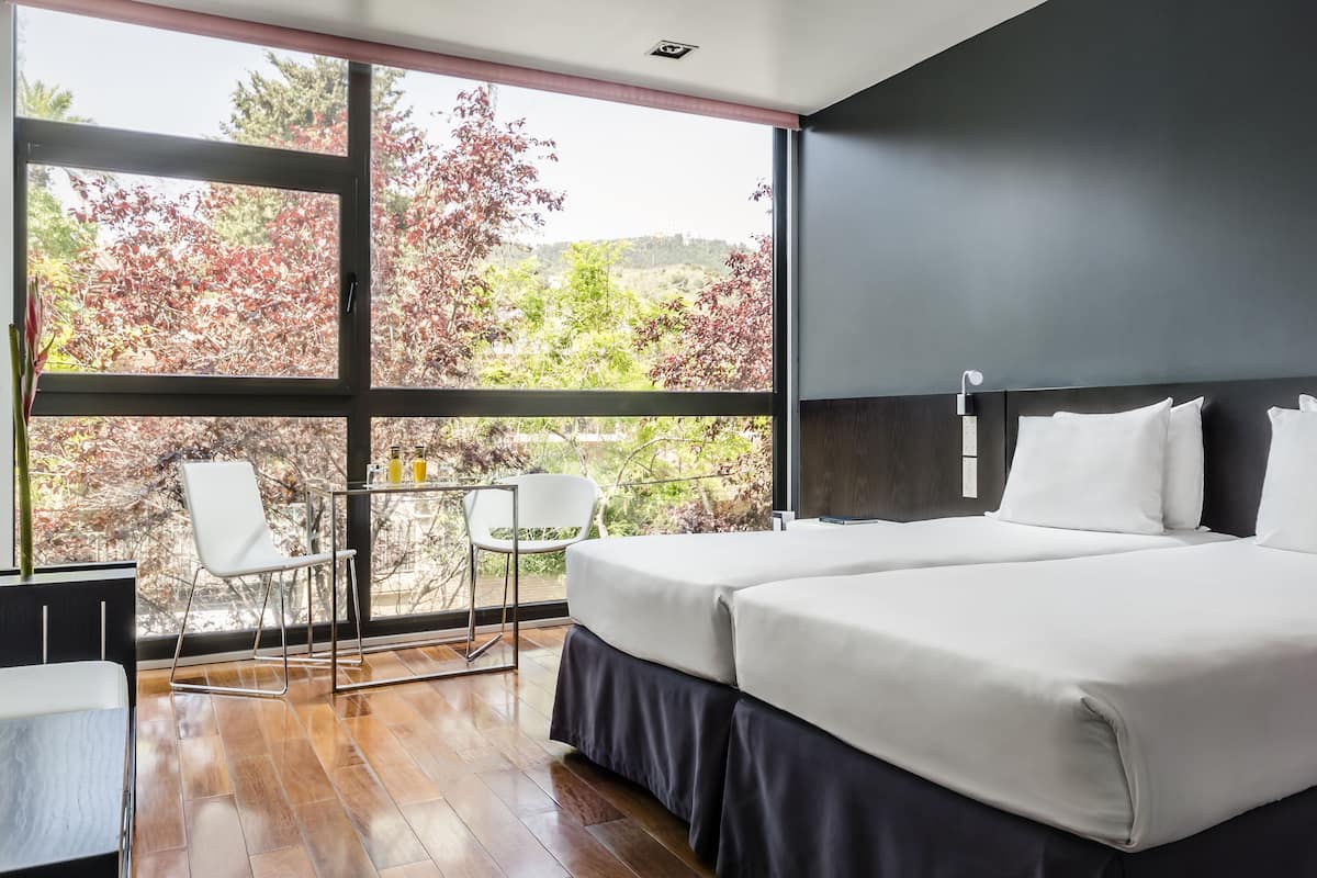 Una habitación de hotel moderna con un ventanal grande, una cama, un escritorio y una silla.