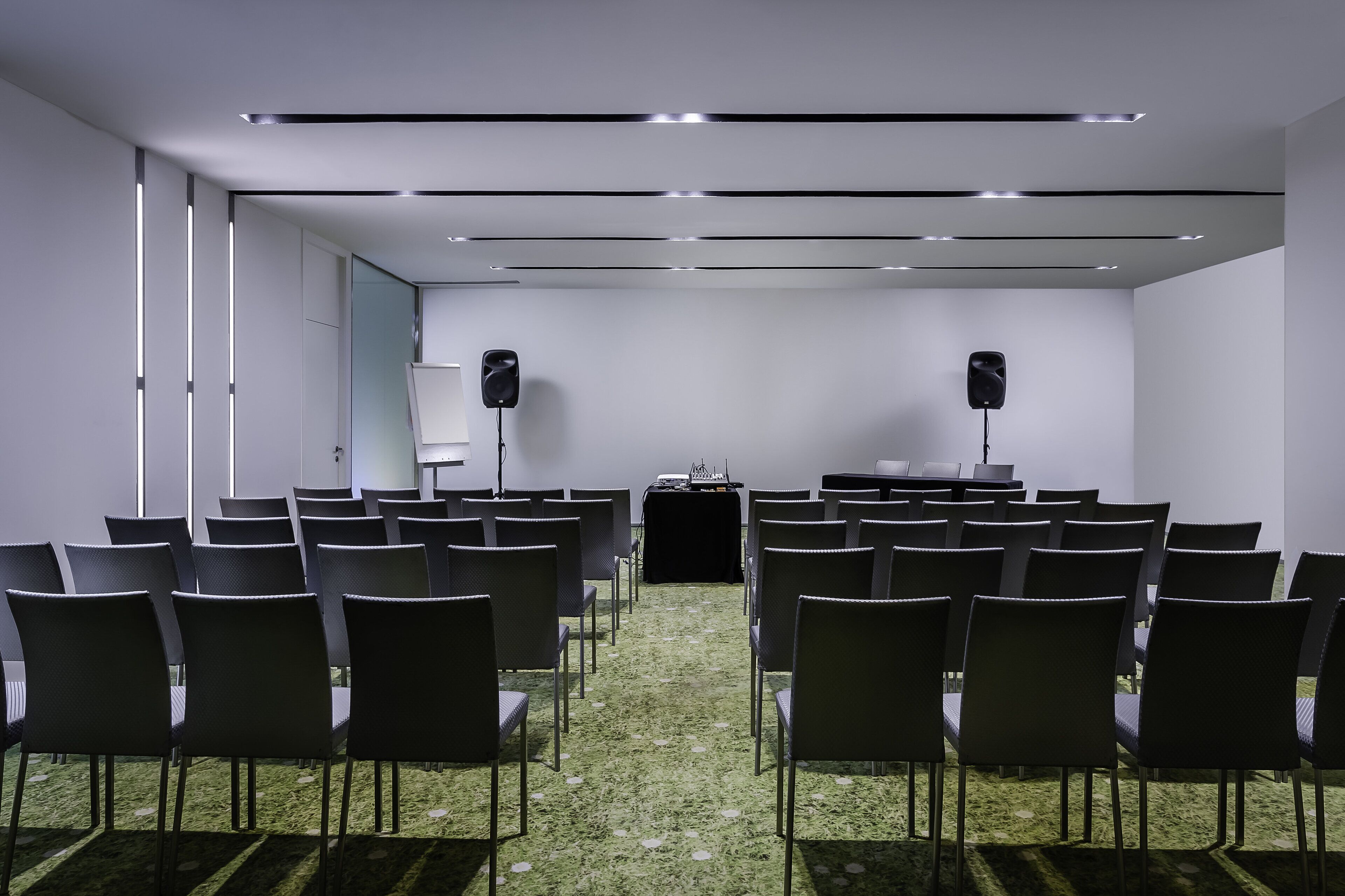 Un salón de conferencias con filas de sillas orientadas hacia un atril, equipado con altavoces y suelo alfombrado.