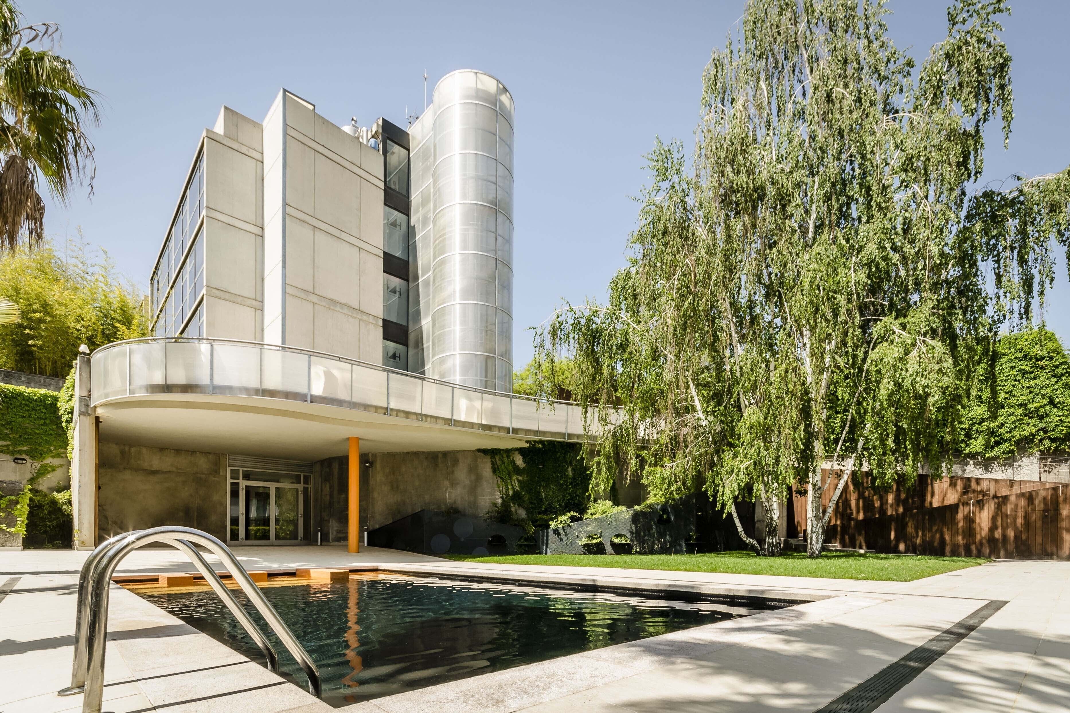 Un edificio moderno con piscina, un paseo techado y una estructura cilíndrica.
