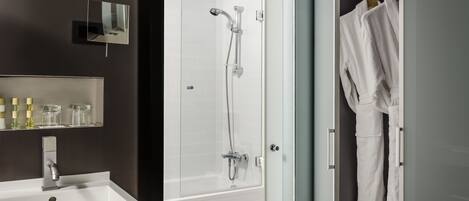 Un baño moderno con un lavamanos blanco, una ducha con cerramiento de vidrio y un vestidor con batas colgadas.
