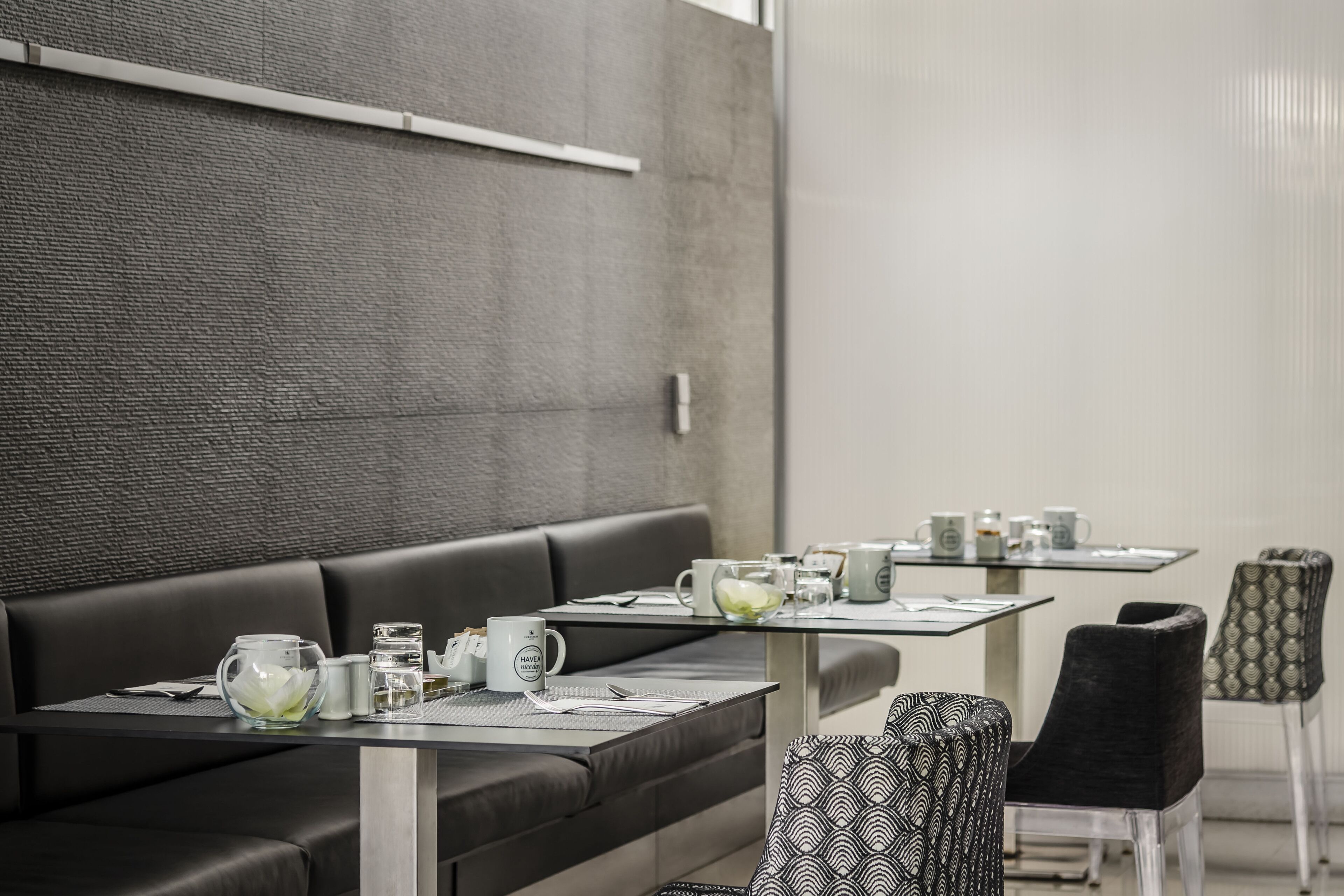 Un moderno vestíbulo de hotel con un sofá de cuero negro, una mesa con superficie de vidrio y una taza blanca, y sillas con diseños.
