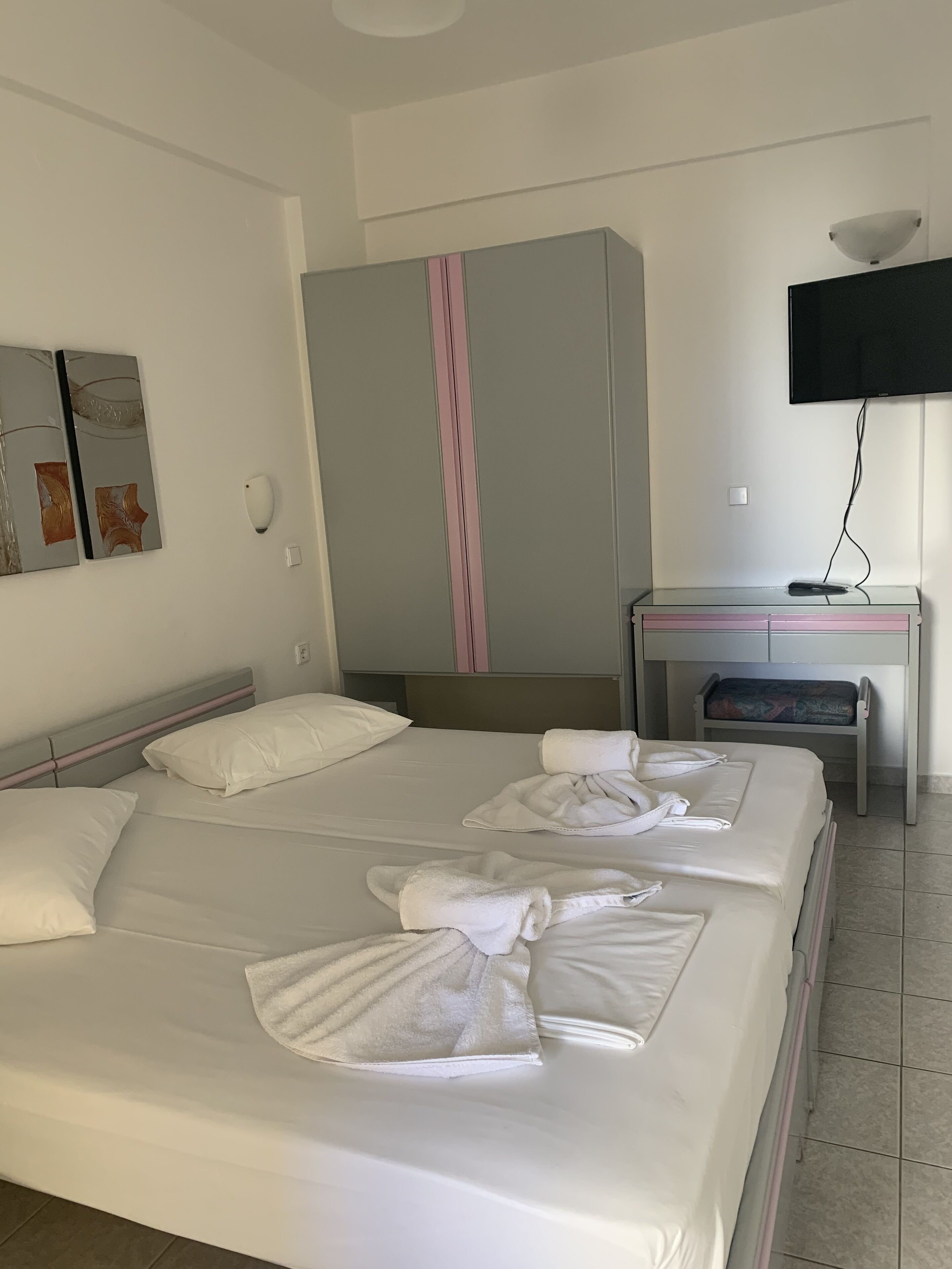 A hotel room with a bed, a desk, a TV, and artwork on the wall.