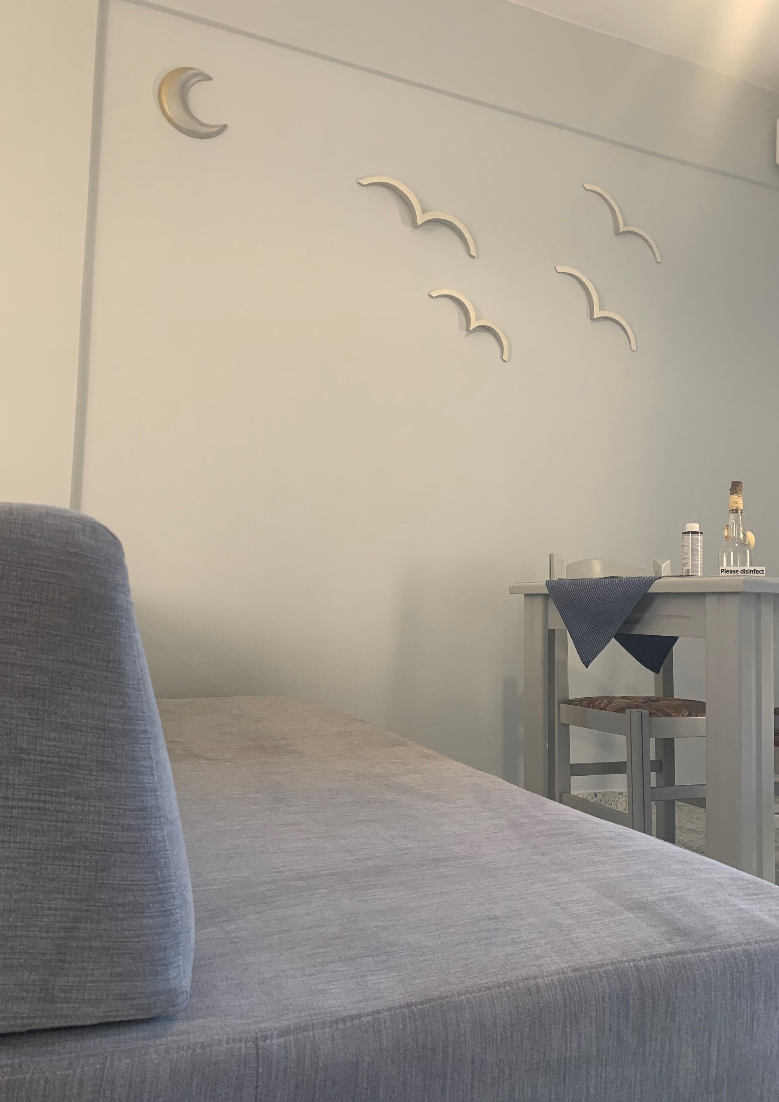 Una habitación con un sofá gris, una mesita con una botella y un cartel, y decoraciones en forma de luna creciente en las paredes.