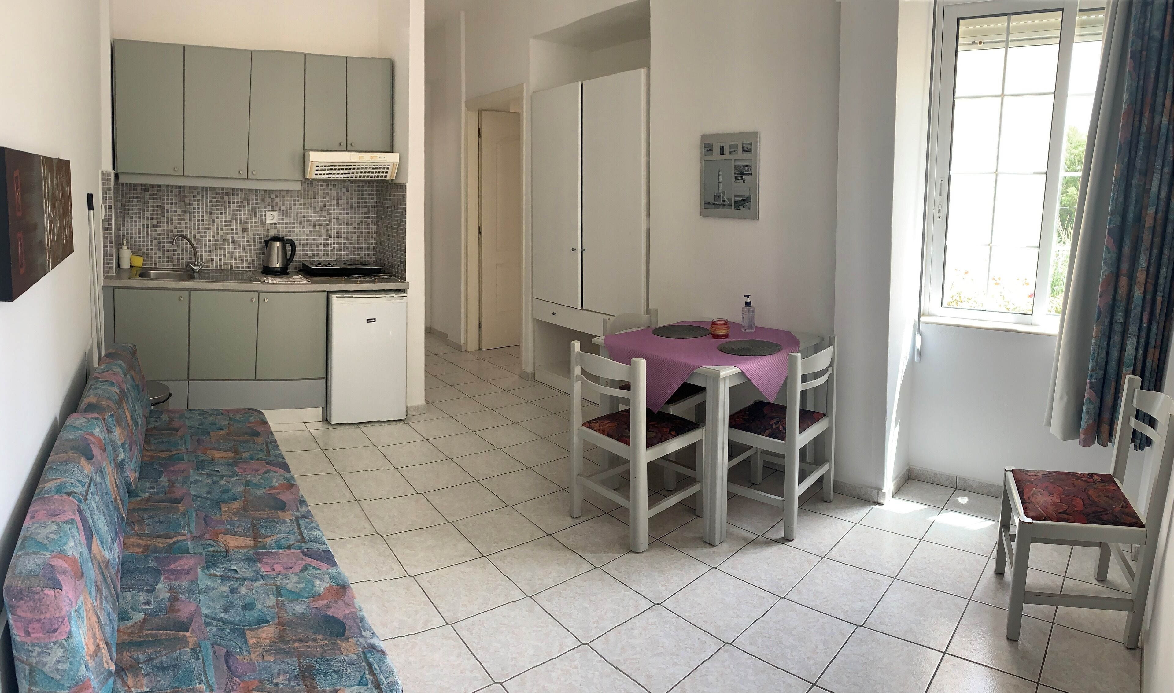 A compact living space with a kitchenette, a dining table with chairs, a sofa, and a window with curtains.