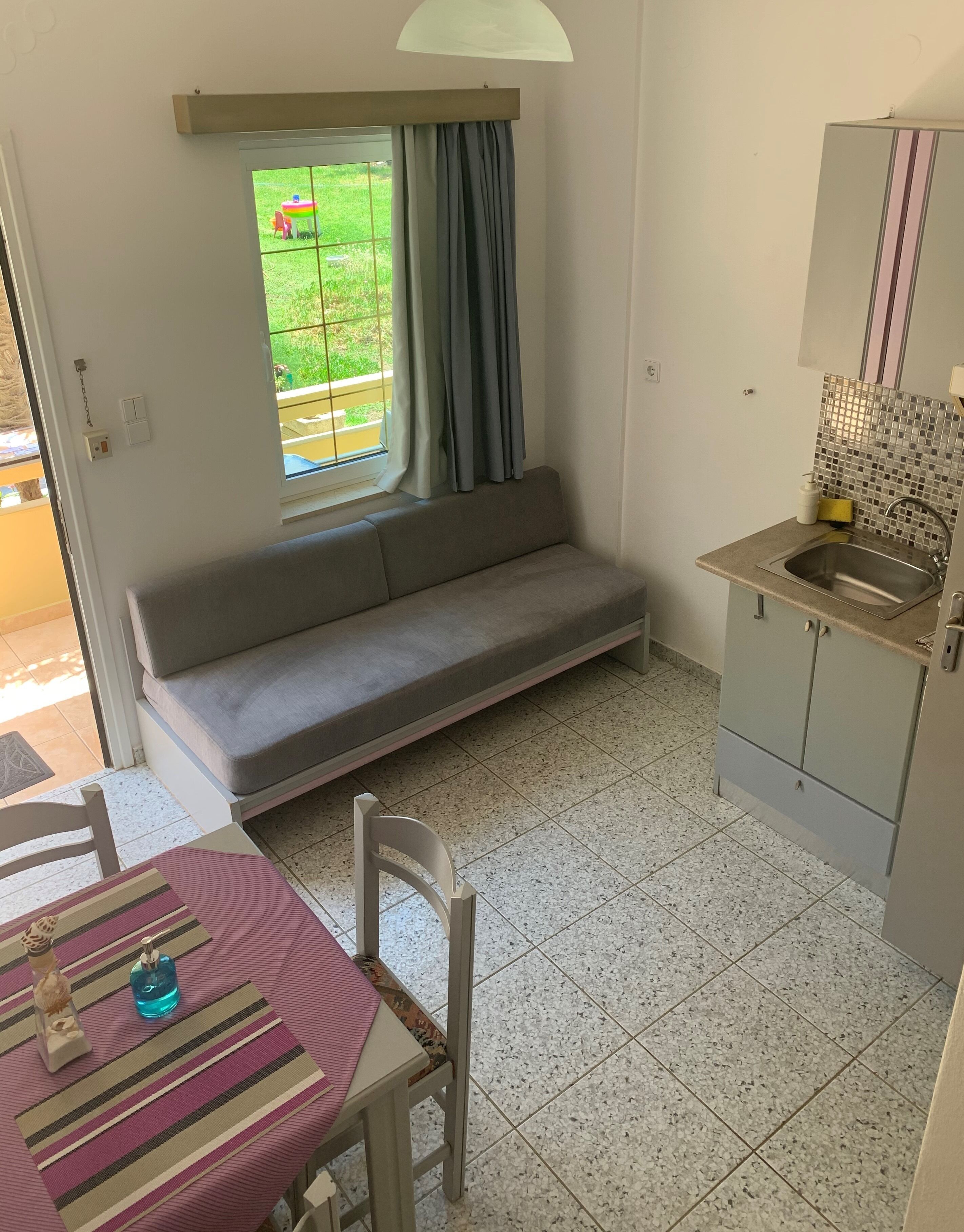A compact kitchen with a built-in sink, a small dining table with chairs, and a sofa near a window with curtains.