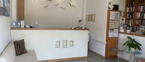 A reception area with a white counter, a sofa with a zebra-patterned pillow, a bookshelf, and a decorative wall with bird silhouettes.