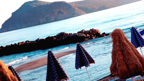Una playa con costas rocosas, una vista despejada del mar y varias sombrillas.