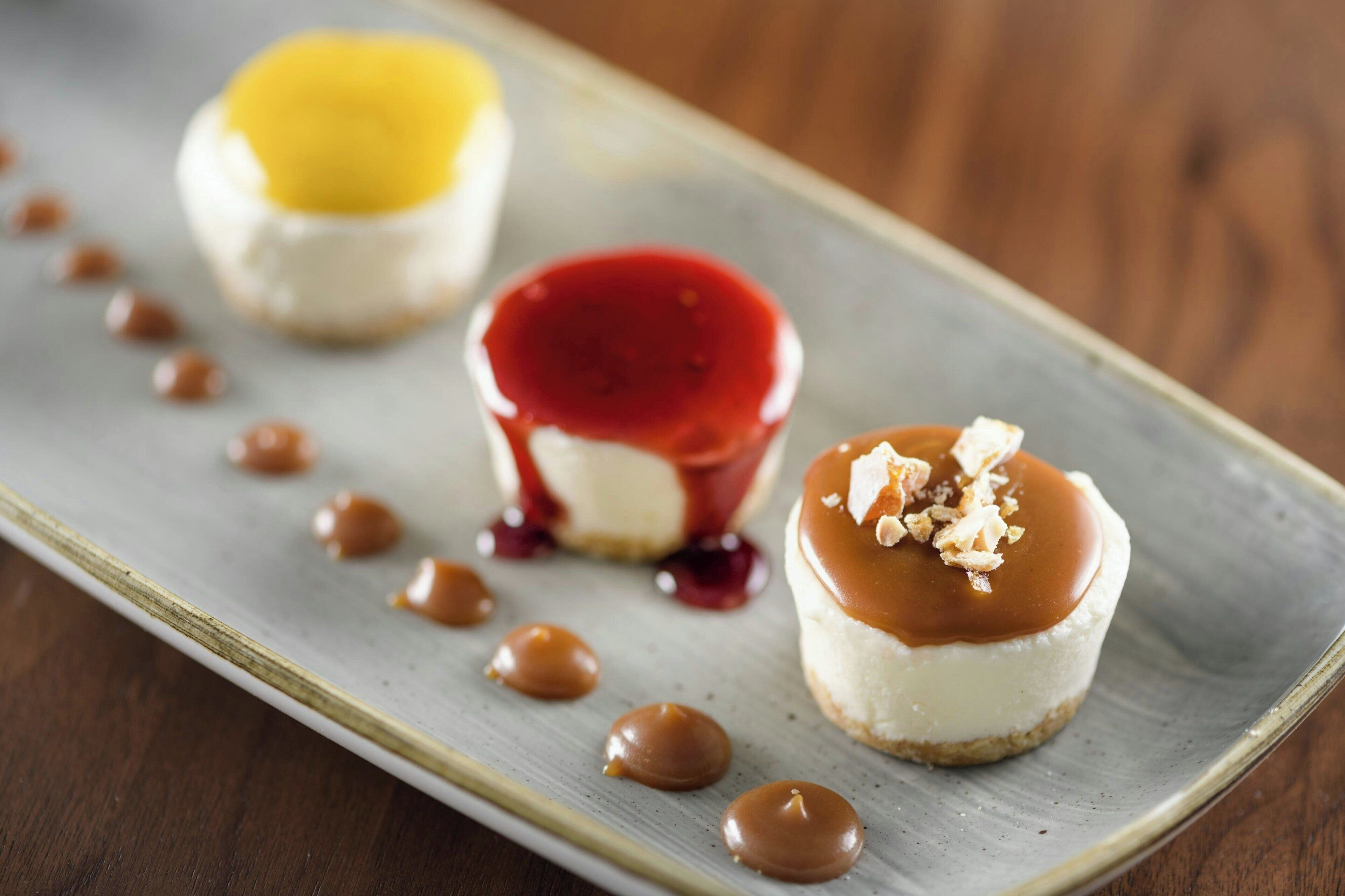 Três sobremesas num prato com calda de caramelo e molho vermelho.