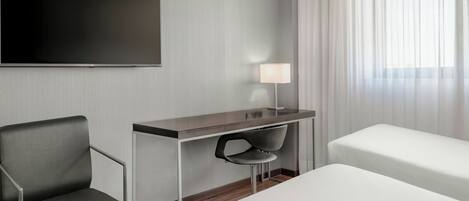 A hotel room with a bed, a desk with a chair, a TV, and a lamp.