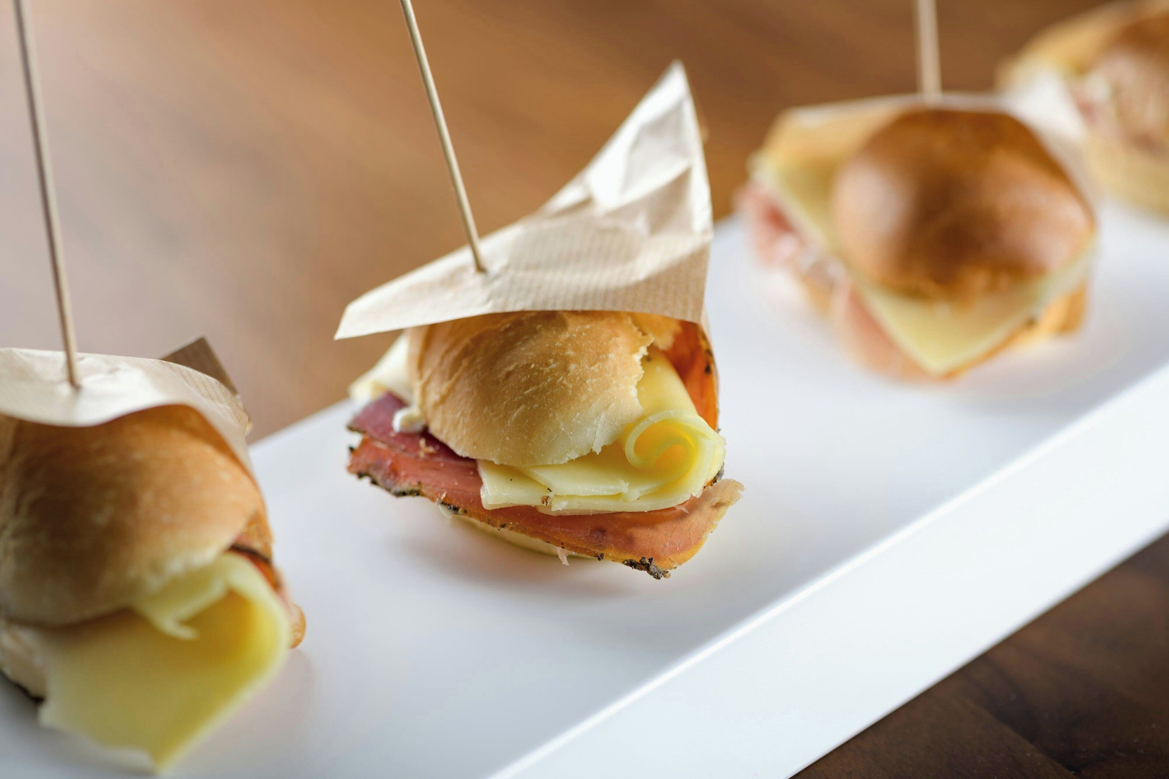 En hvid, rektangulær tallerken med tre sandwiches, hver holdt fast med en cocktailpind.