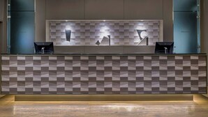 Un área de recepción con pared de diseño geométrico, un mostrador de recepción y dos sillas negras.