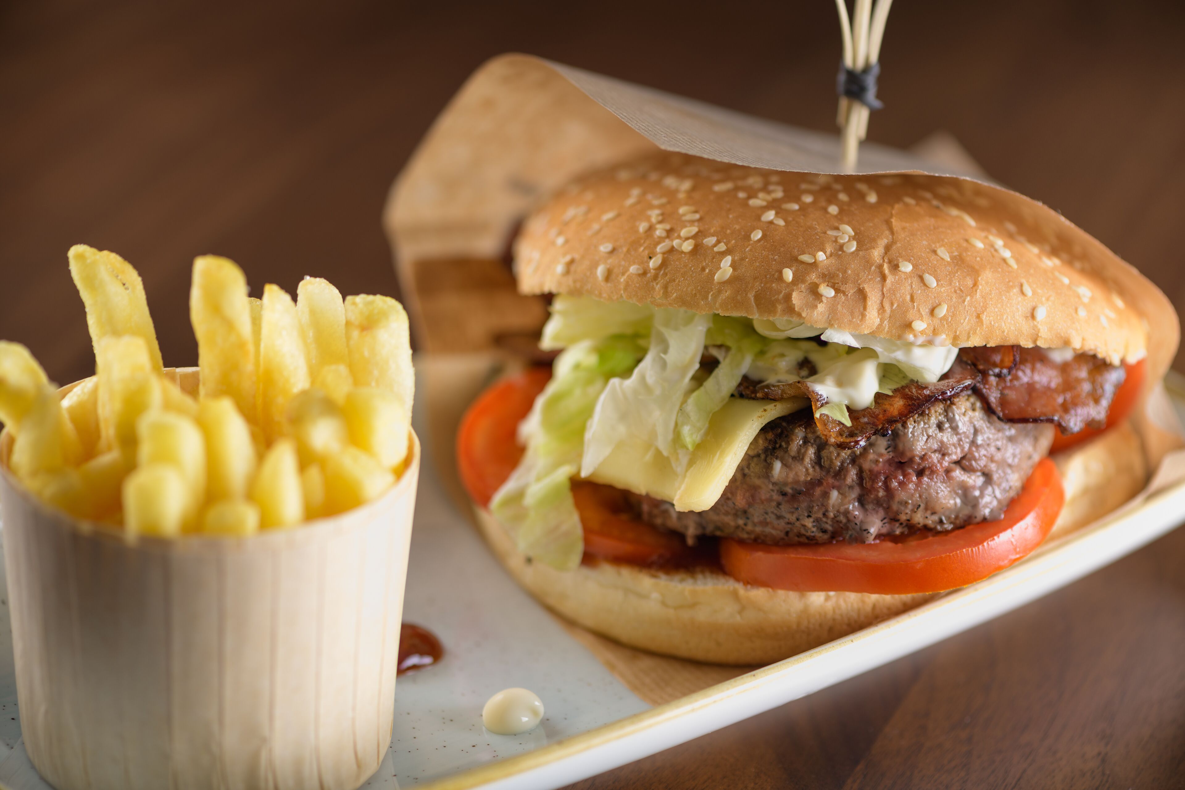 Ein Burger mit Salat, Tomate und einem Sesambrötchen, dazu eine kleine Portion Pommes.