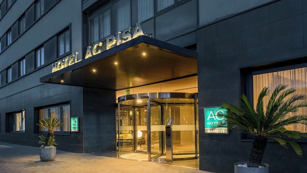 Entrada de un hotel con puerta de cristal, un cartel sobre la puerta y plantas en macetas en la acera.