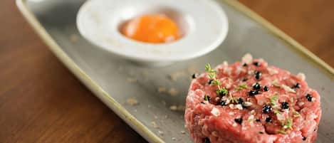 A dish of raw ground meat garnished with herbs and black pepper, served on a rectangular plate with a small bowl of egg yolk.