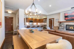 A modern kitchen with wooden cabinets, a central island, and a dining area with a wooden table and benches. - East West Hospitality Tahoe (Truckee)
