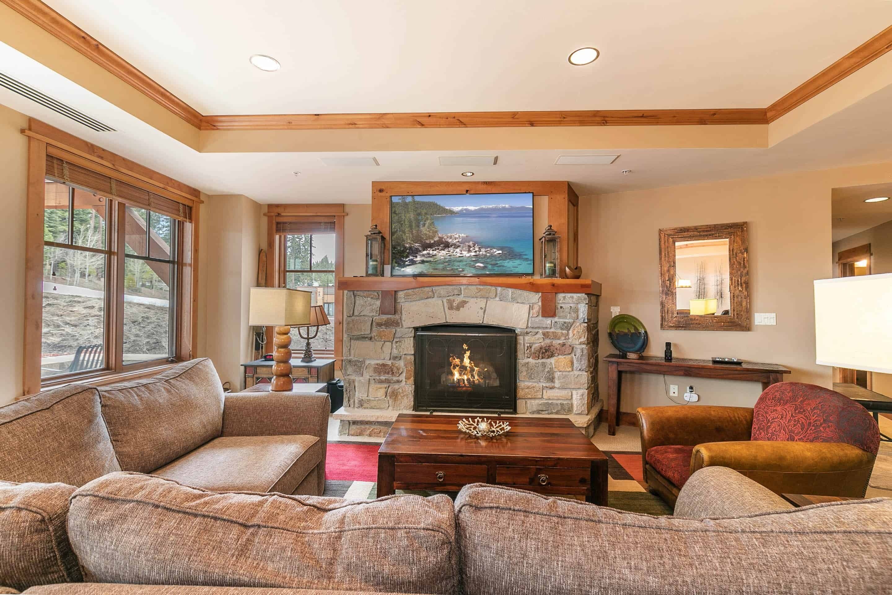 A living room with a stone fireplace, a large TV mounted above it, and a cozy seating area with a sofa and armchairs.