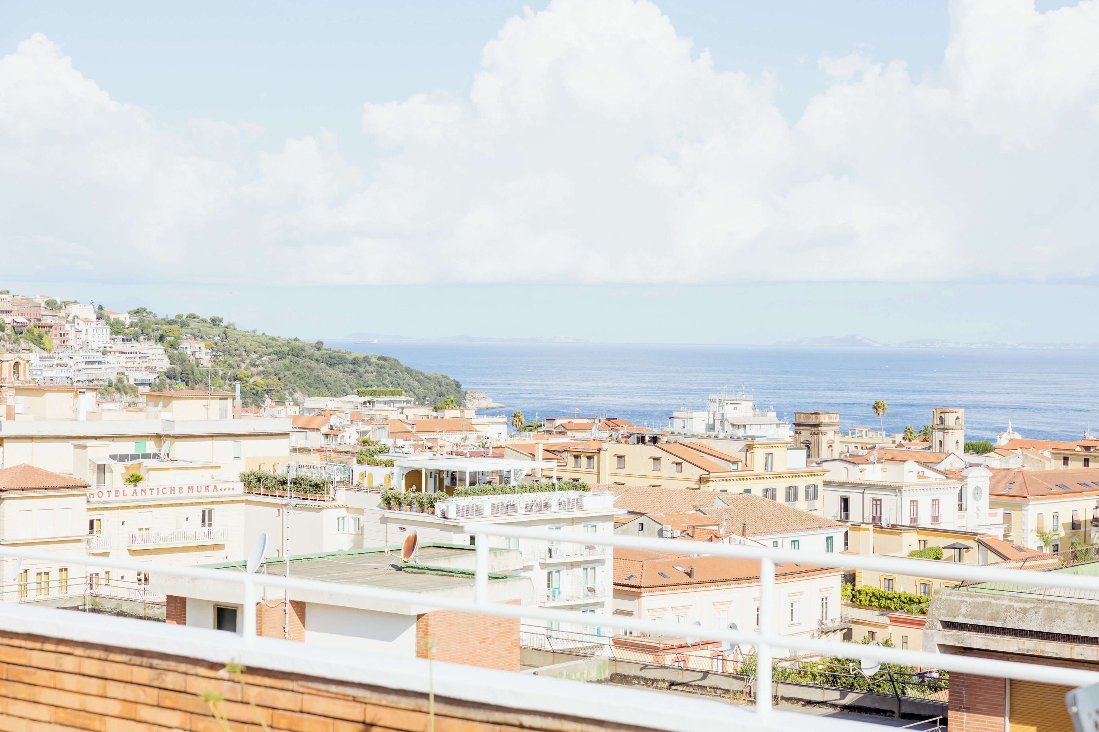 Uma cidade costeira com edifícios, céu claro e o mar ao fundo.