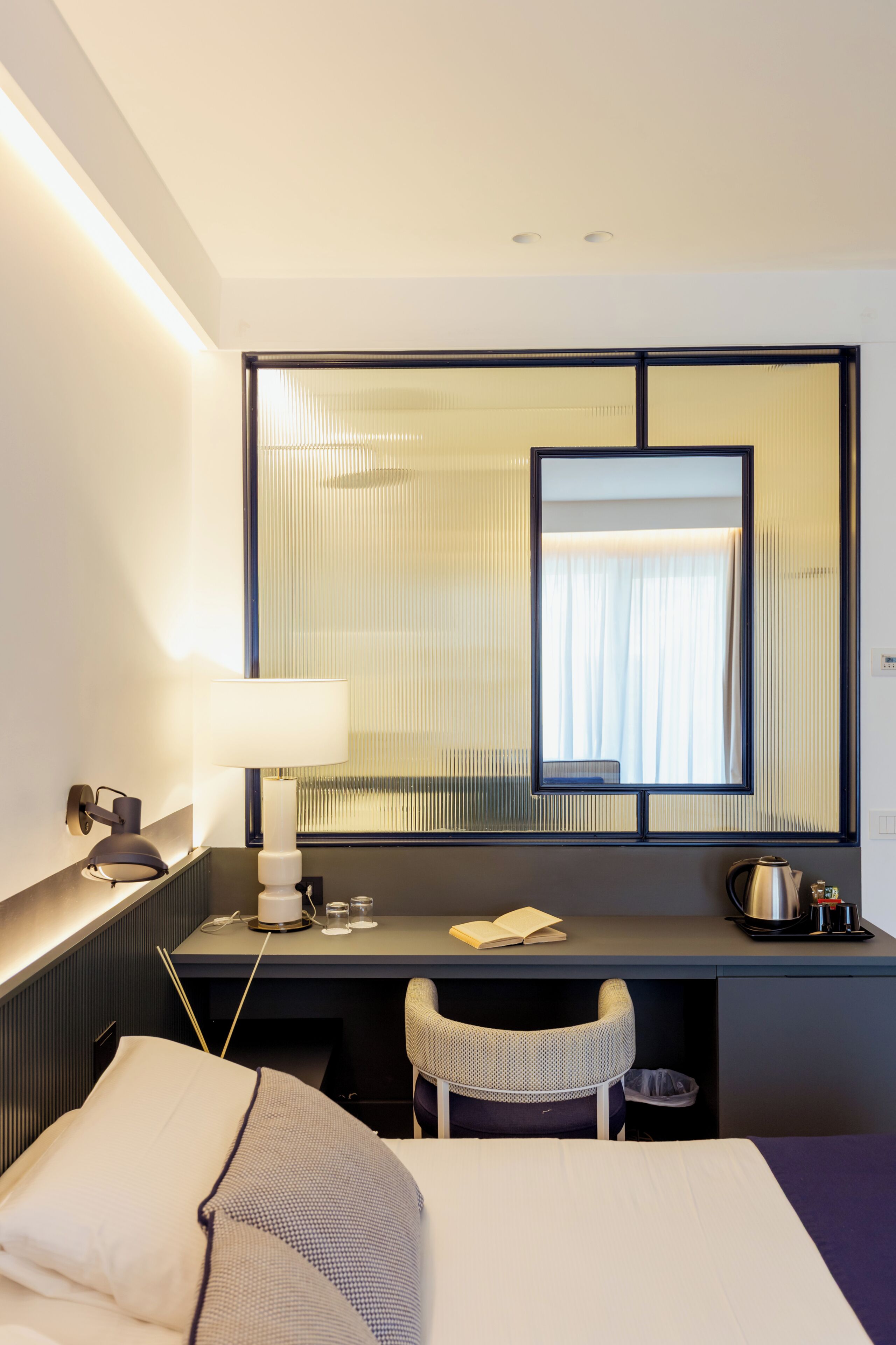 Habitación de hotel con cama, escritorio con lámpara, silla, mesita y ventana con persianas.
