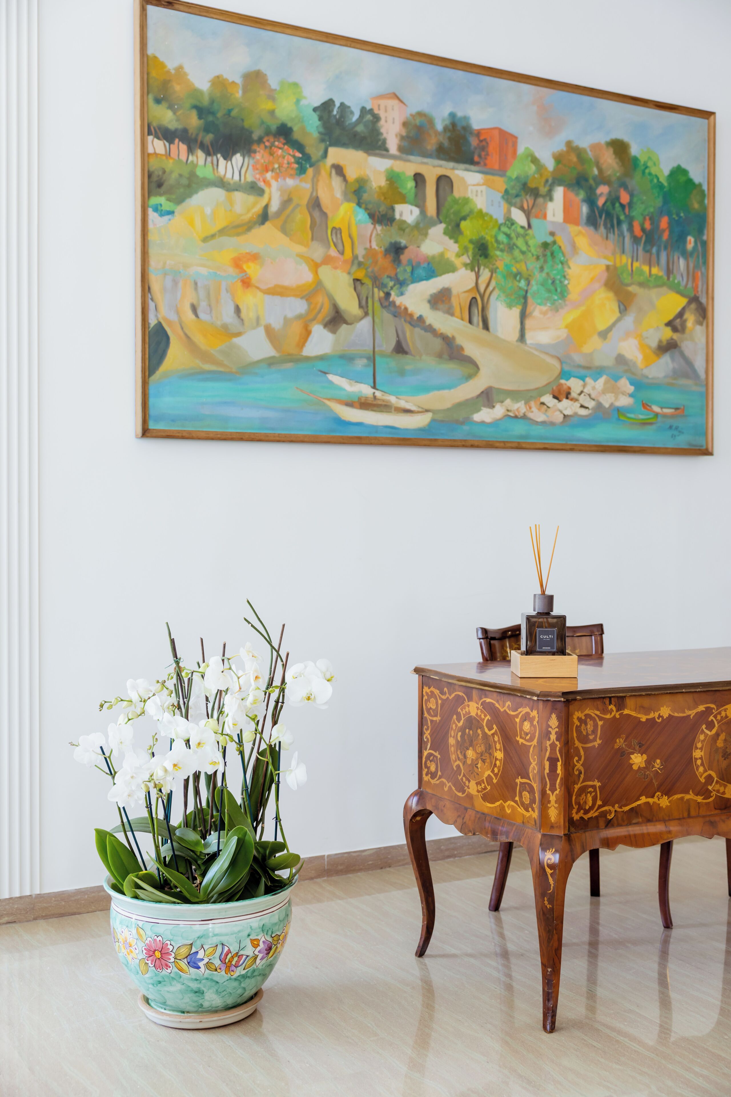 A painting, a table with a vase of flowers, and a wooden cabinet.