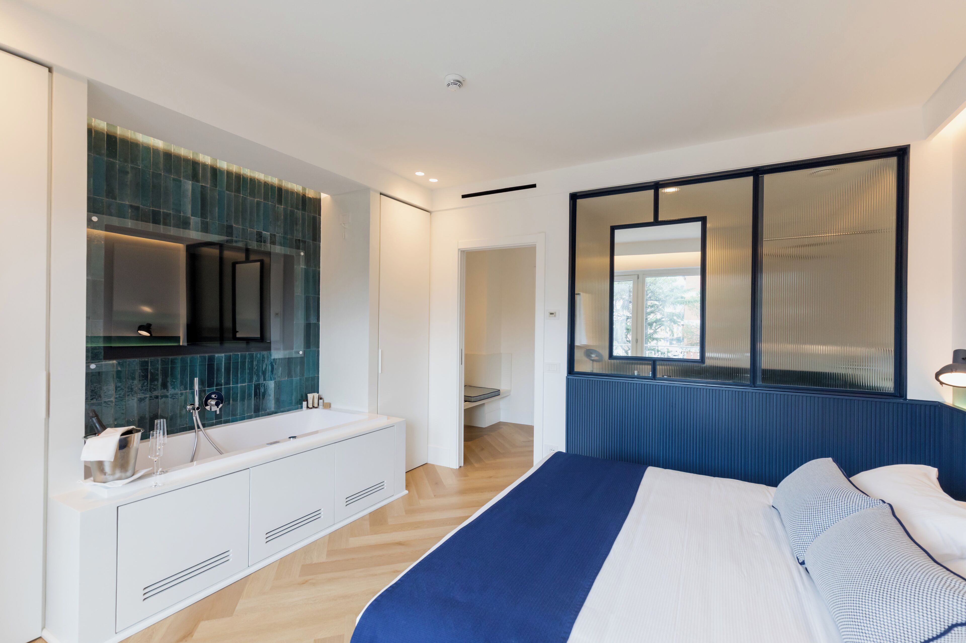 A modern bedroom with a large bed, a built-in vanity with a mirror, and a view of the outdoors through a window.