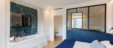 Une chambre moderne avec un grand lit, une coiffeuse intégrée avec un miroir et une vue sur l’extérieur par une fenêtre.