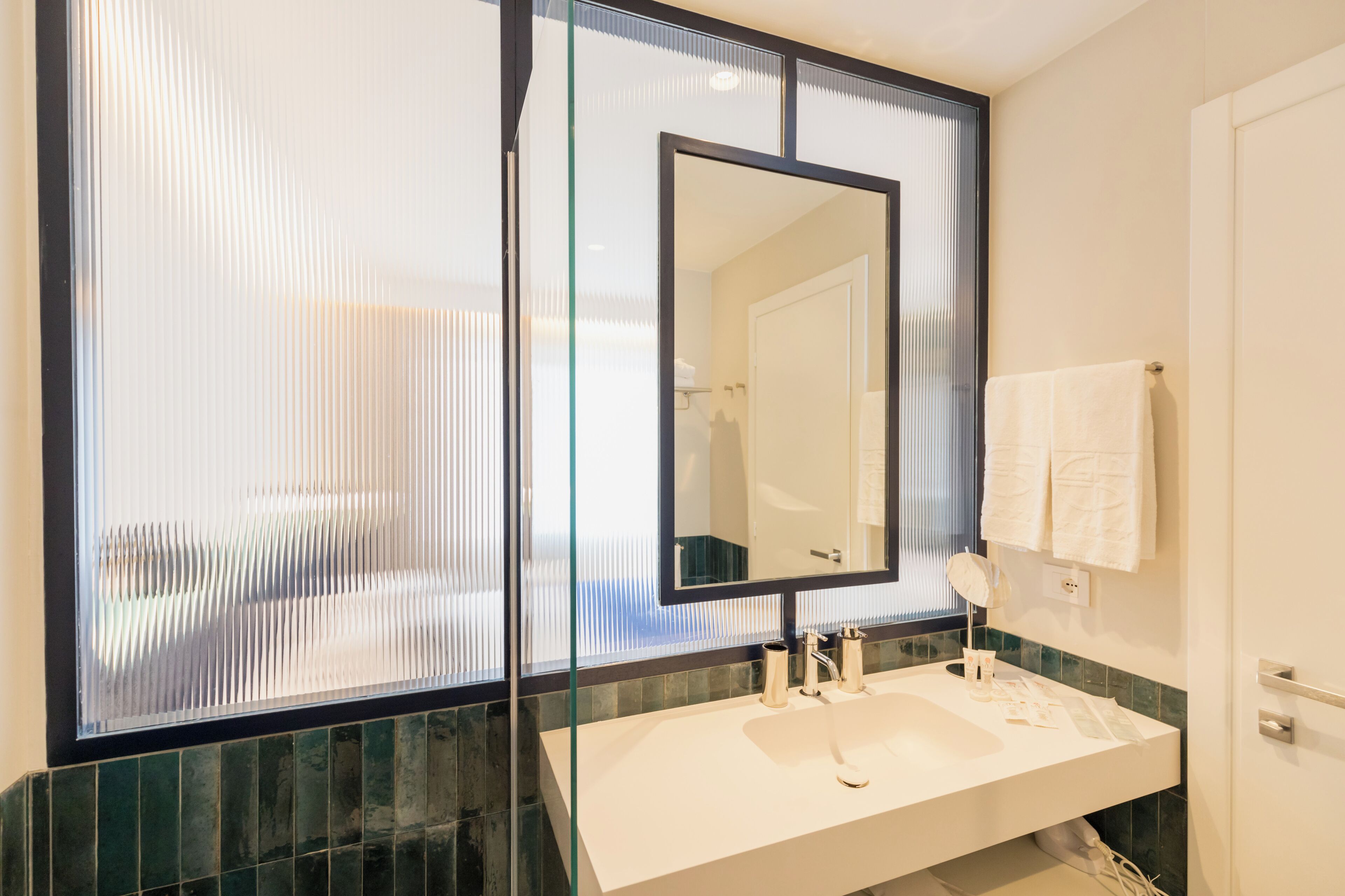 Un baño moderno con un espejo grande, un lavabo blanco y un separador de vidrio.
