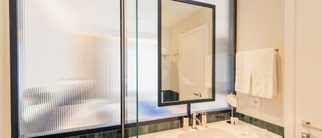 Un baño moderno con un espejo grande, un lavabo blanco y un separador de vidrio.