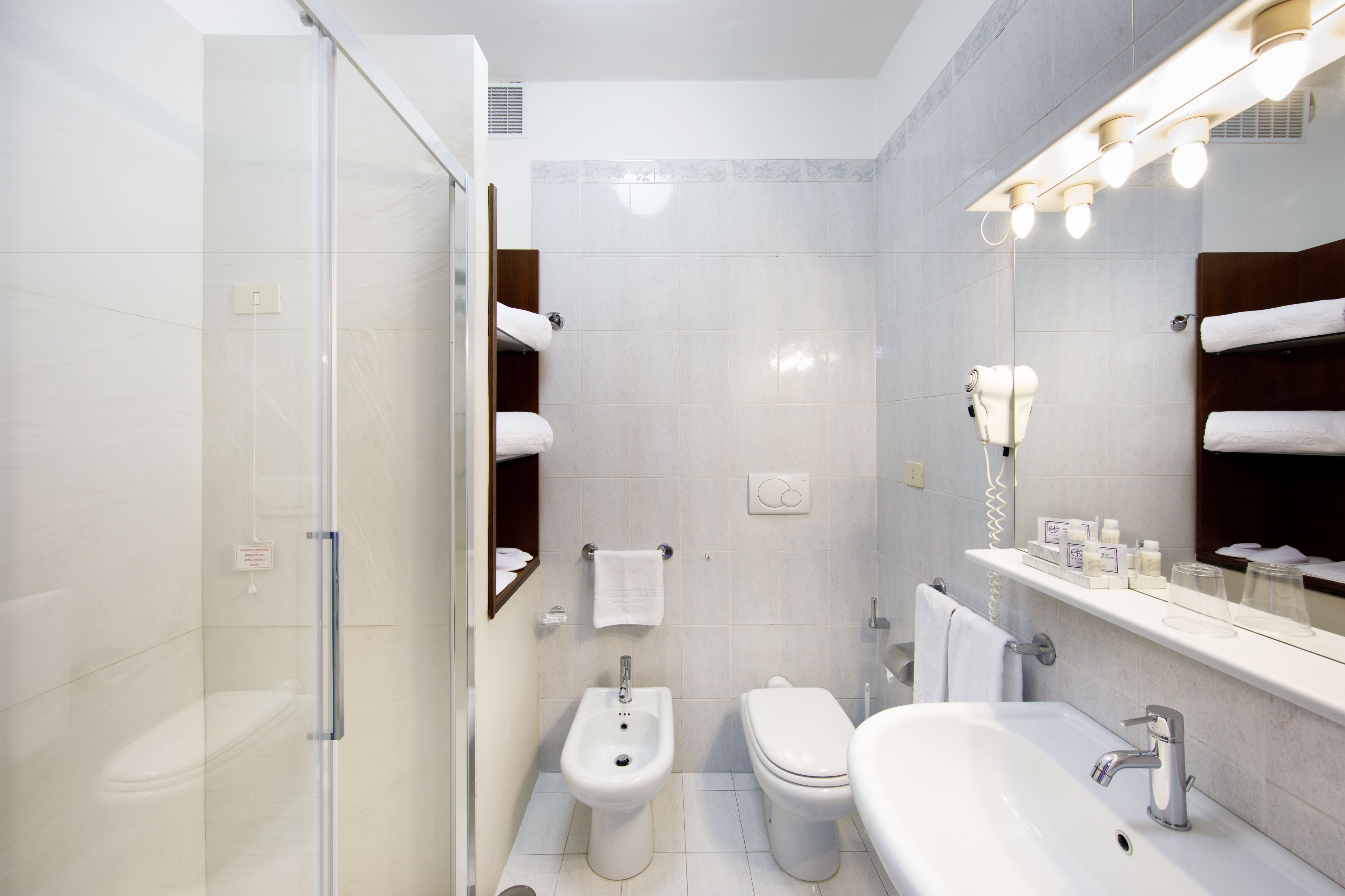 Un baño moderno con cabina de ducha de vidrio, un bidé, un inodoro y un lavamanos con espejo.