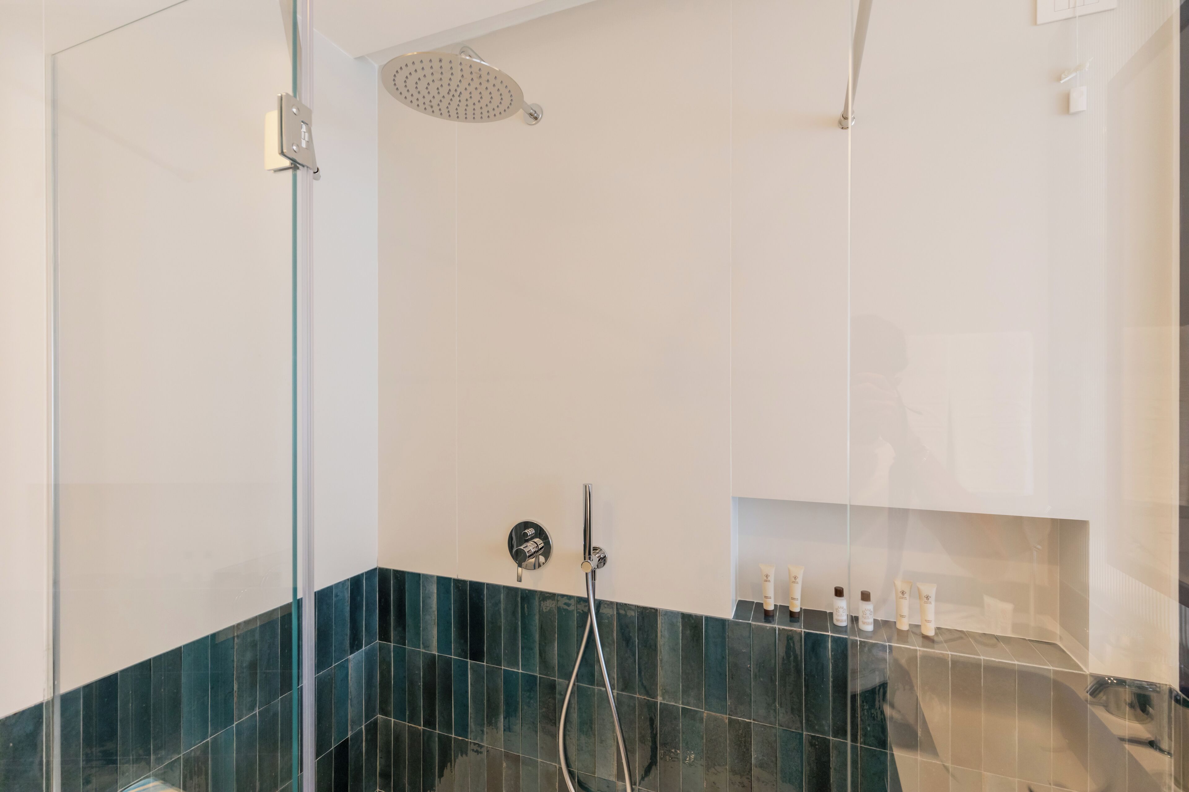 A modern bathroom with a glass shower enclosure, a handheld showerhead, and a wall-mounted control panel.