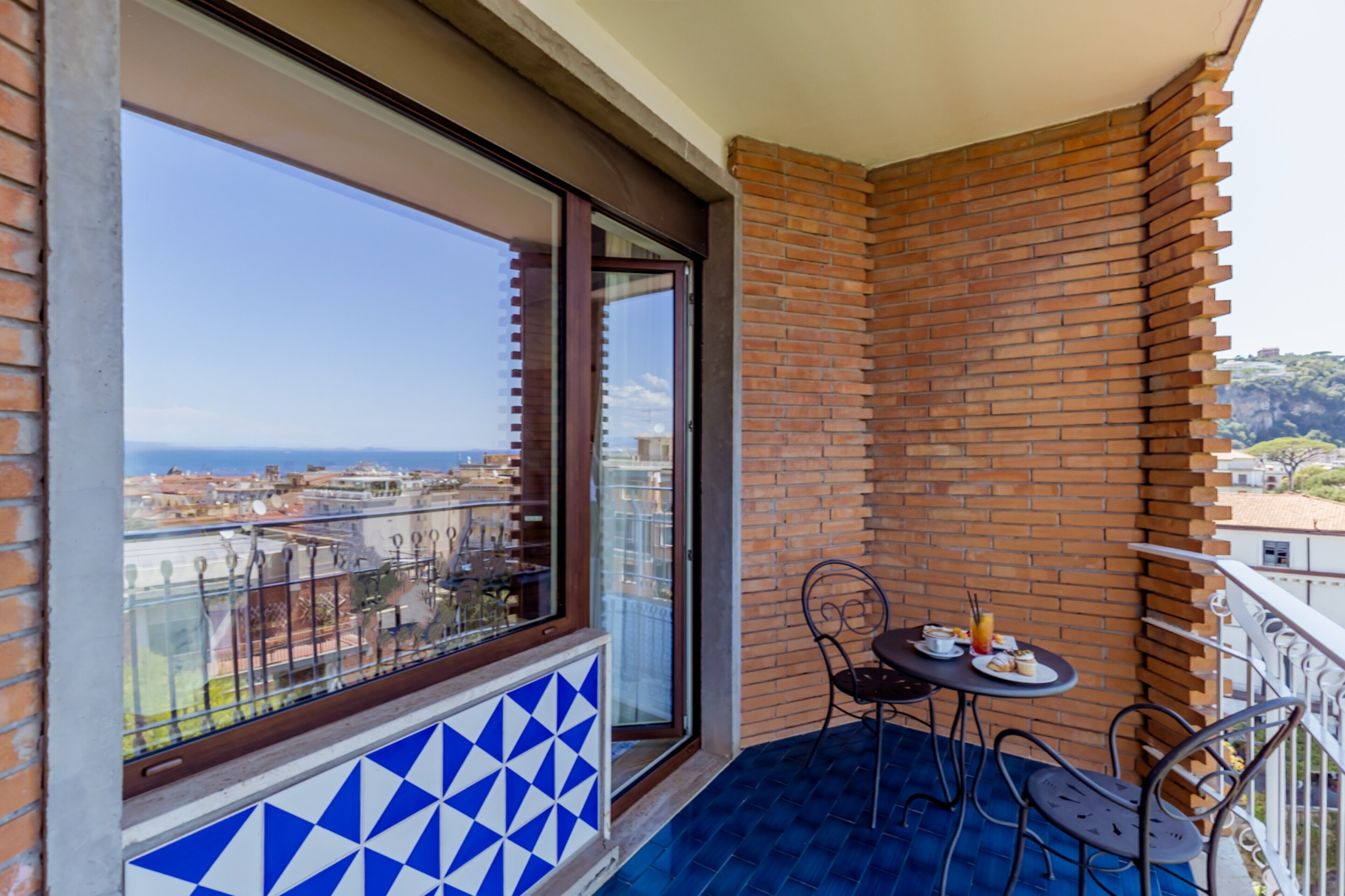 A balcony with a view of the city, a table with chairs, and a tiled floor.