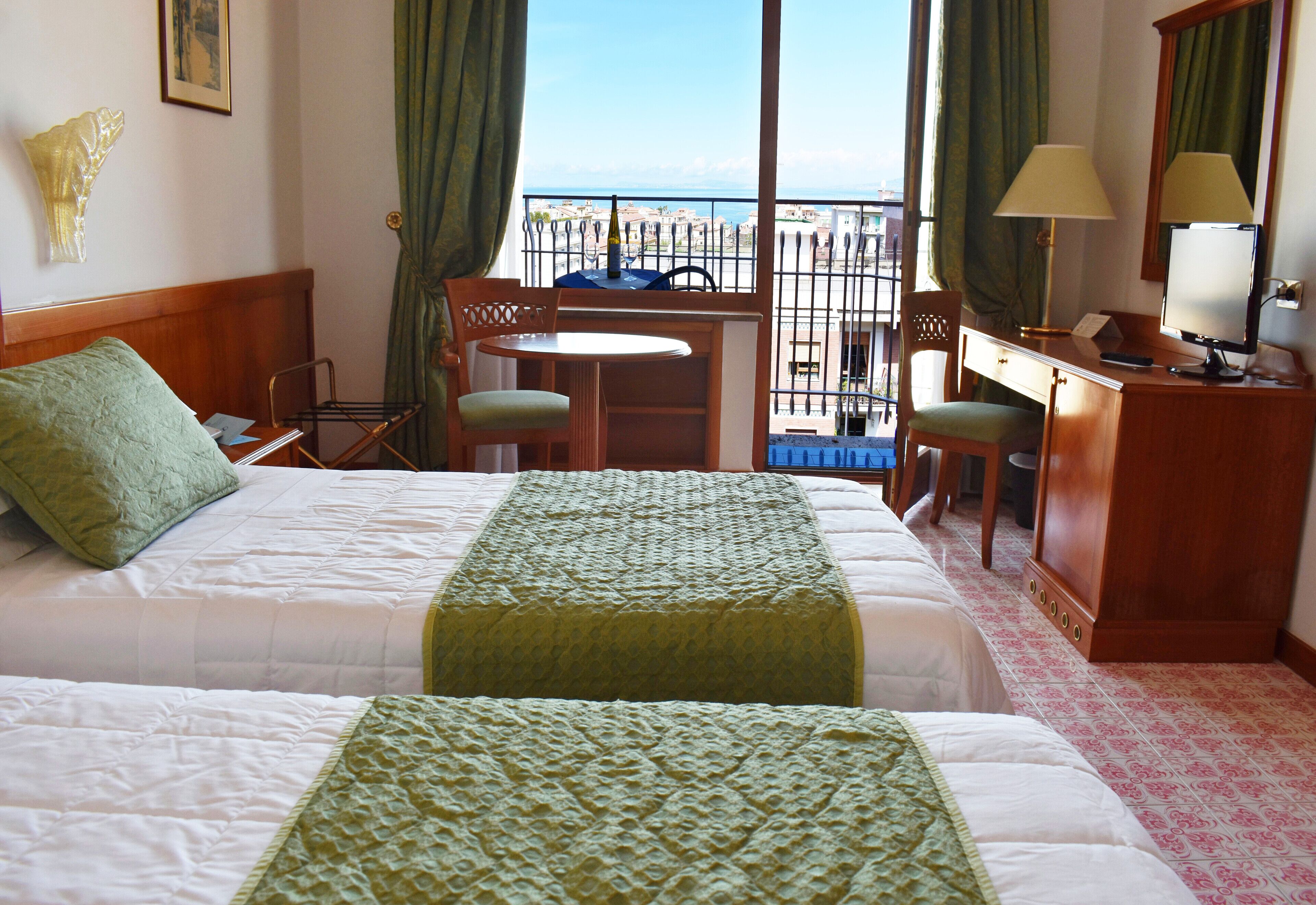 Een hotelkamer met twee bedden, een bureau, een stoel, een kleine tafel en uitzicht op zee.