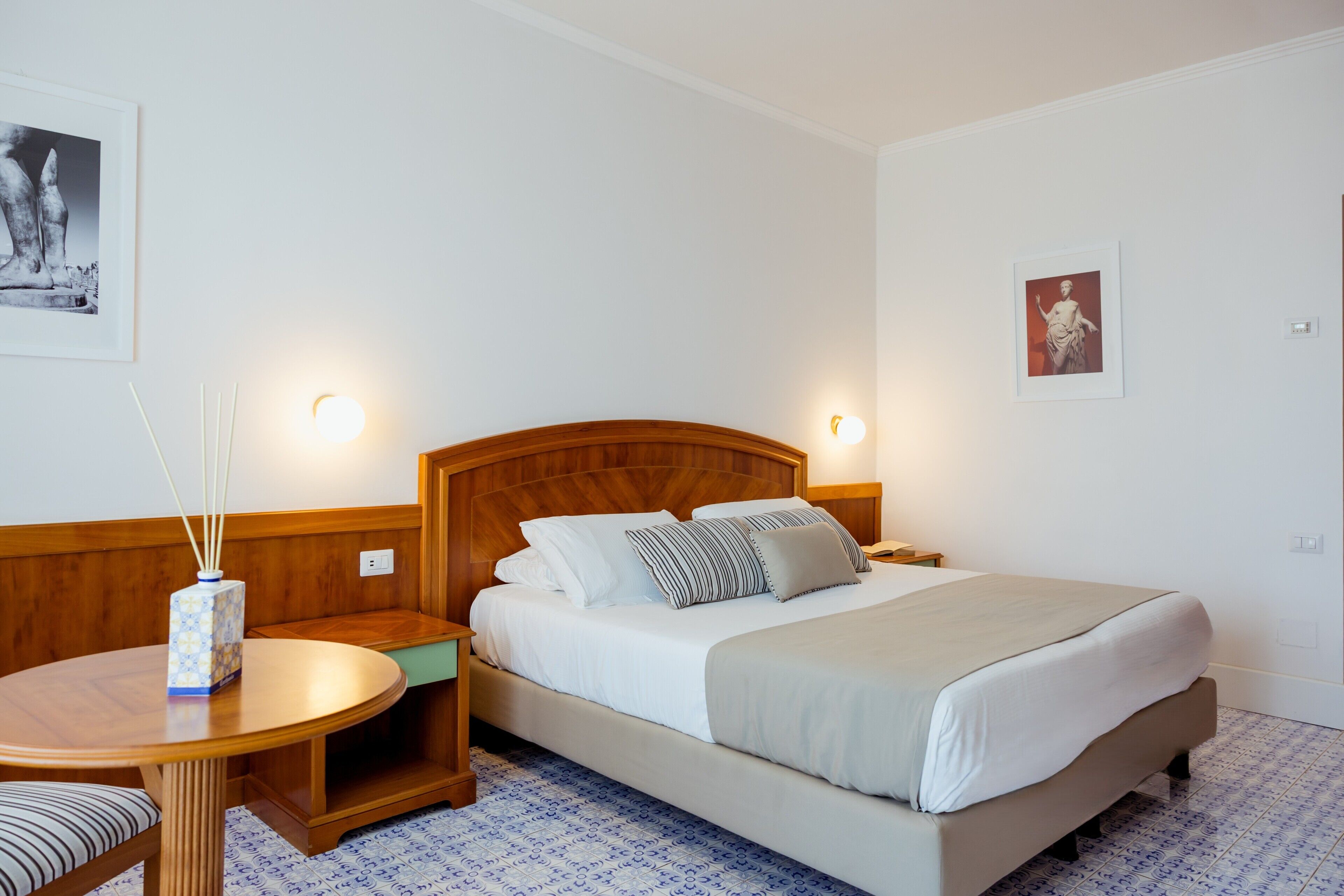 Una camera d'albergo con un letto, comodini, un tavolo rotondo e due luci a parete.