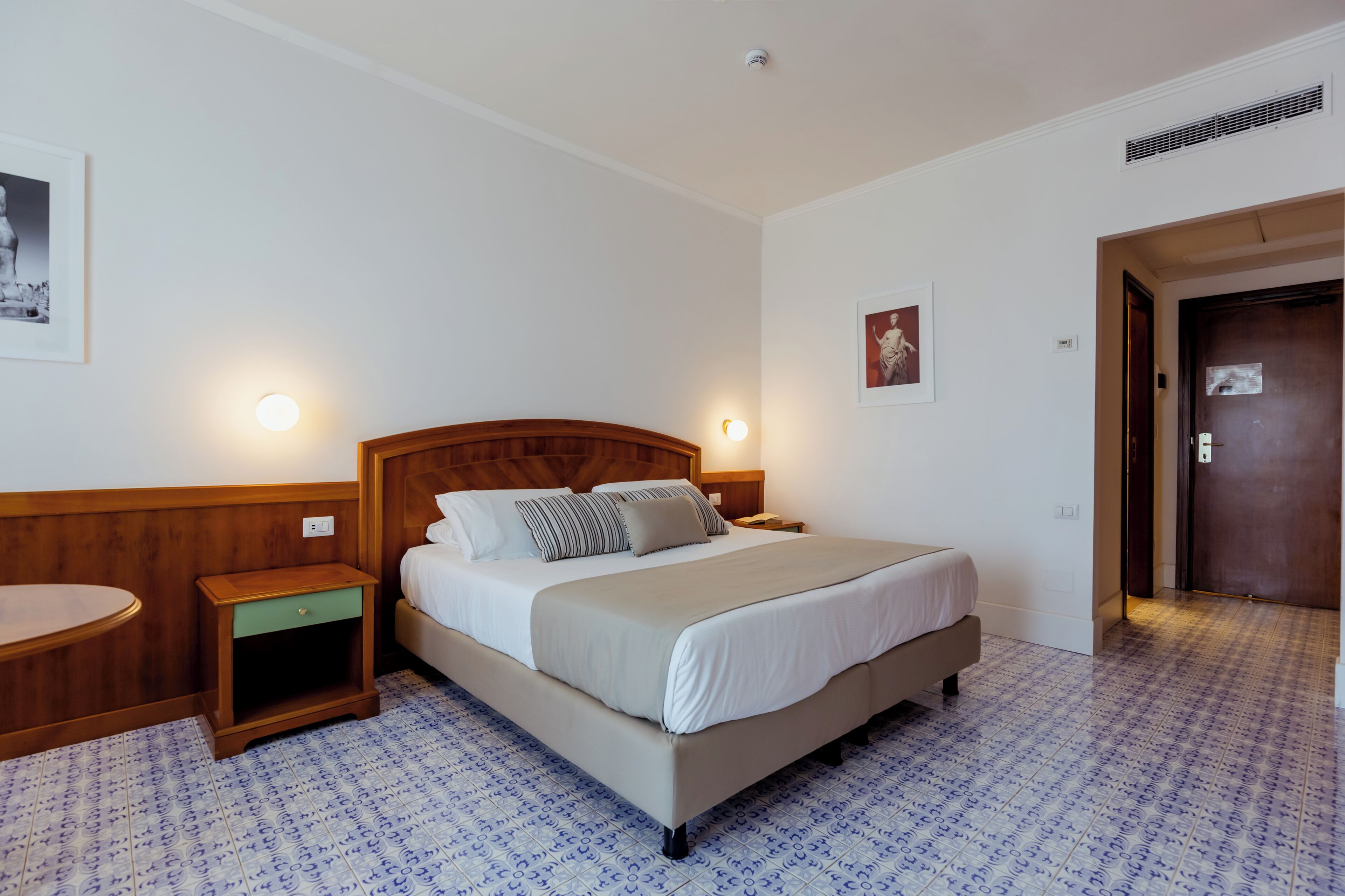 A hotel room with a single bed, bedside tables, a nightstand, a wall-mounted light, and a door.