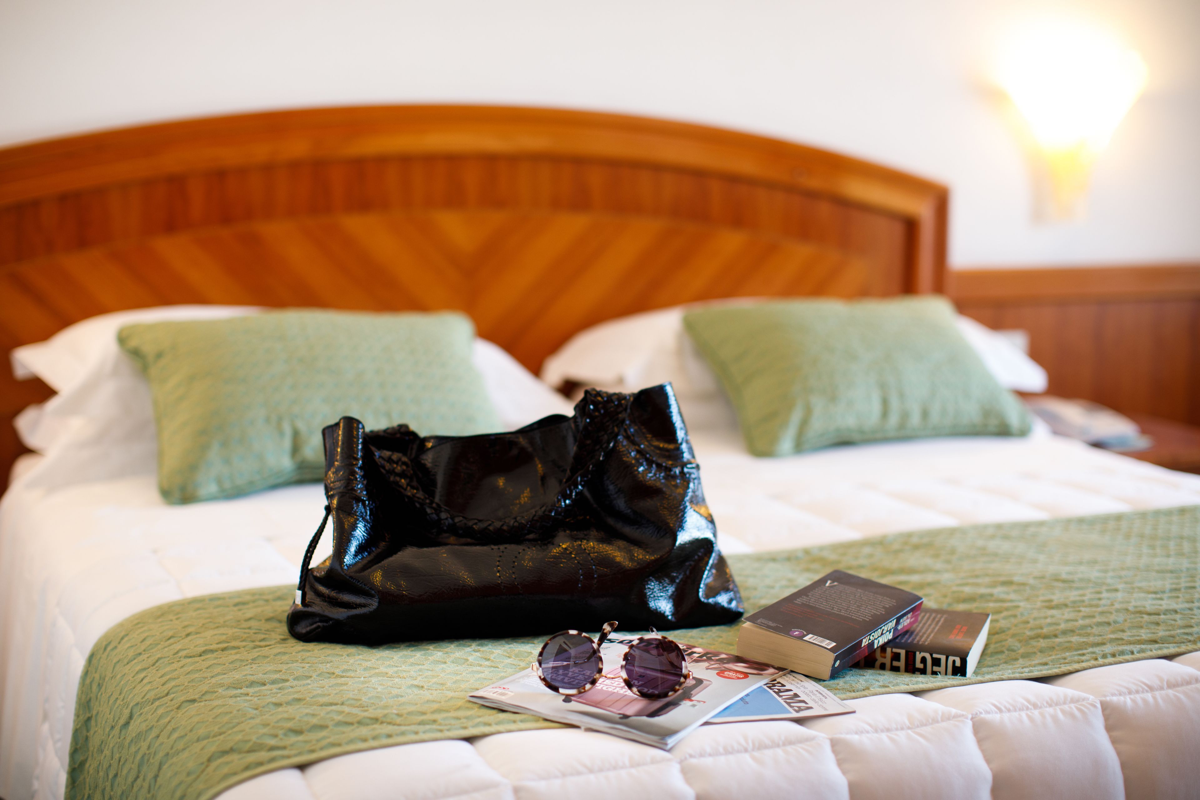 A neatly made bed with a green pillow, a black bag, and a magazine on it.