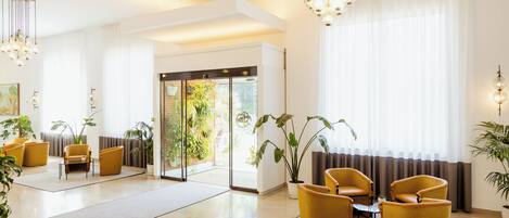 A spacious lobby with a modern design, featuring a seating area with yellow chairs, a coffee table, and a large window with curtains.