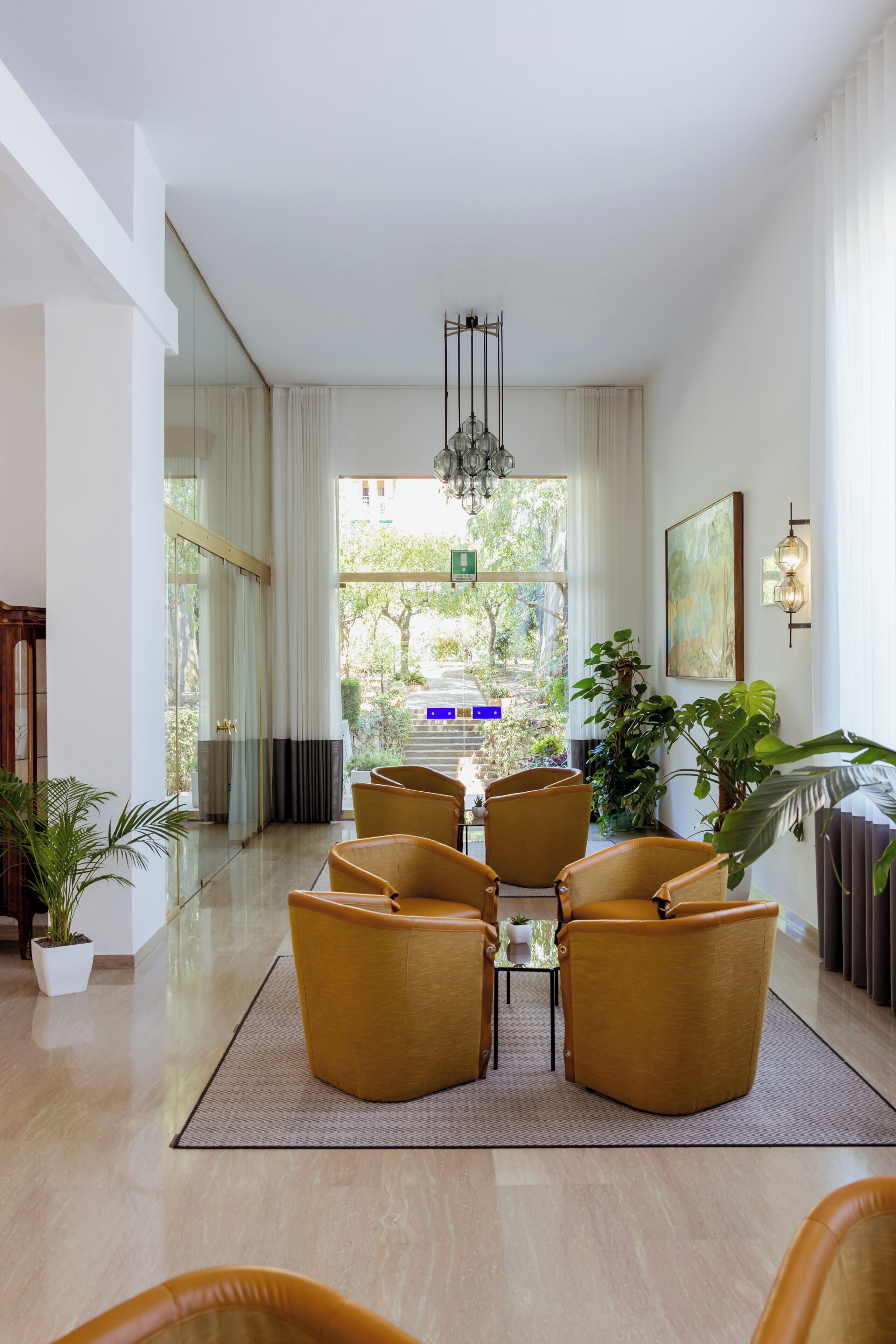 A hotel lobby with a reception desk, seating area, large windows, and indoor plants.
