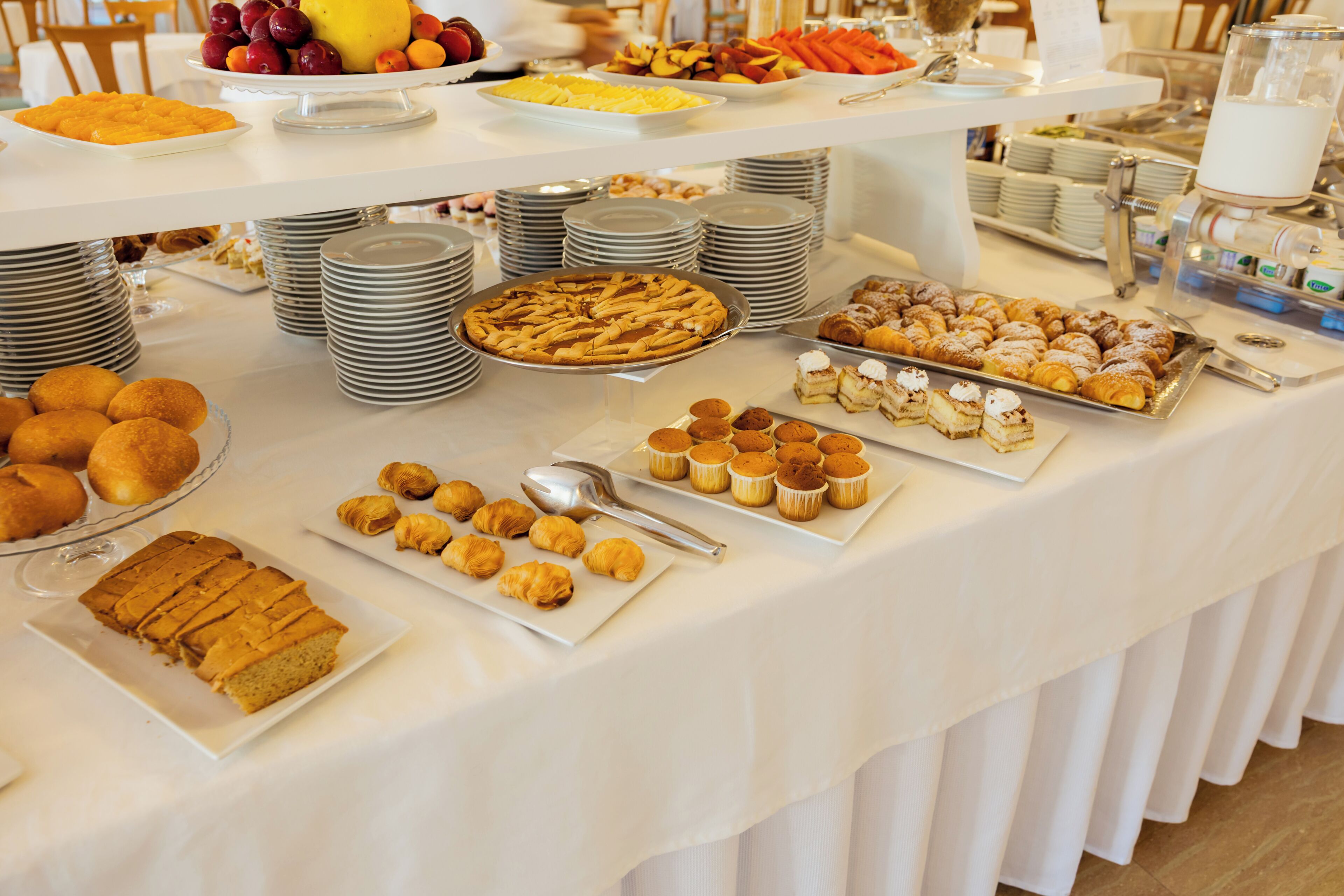 A buffet table with various food items and stacked plates.