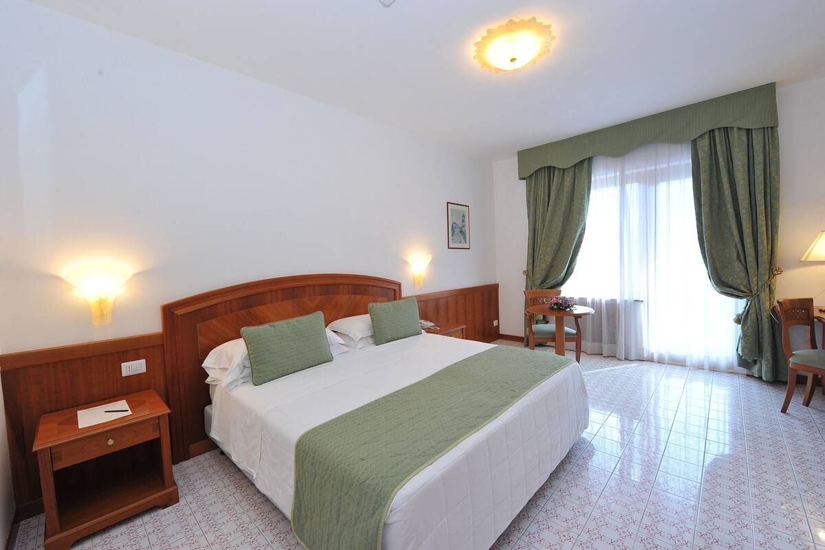 Ein Hotelzimmer mit einem großen Bett, einem Nachttisch, einem Schreibtisch und einem Sessel.