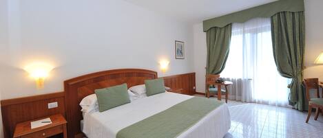 A hotel room with a large bed, a nightstand, a desk, and a chair.