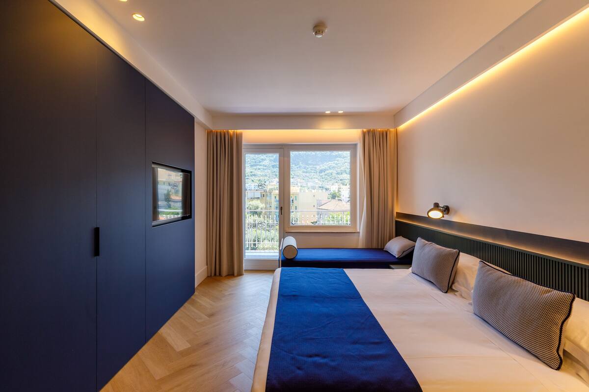 Une chambre d’hôtel moderne avec un grand lit, un petit canapé, une fenêtre avec des rideaux et une vue sur la ville.