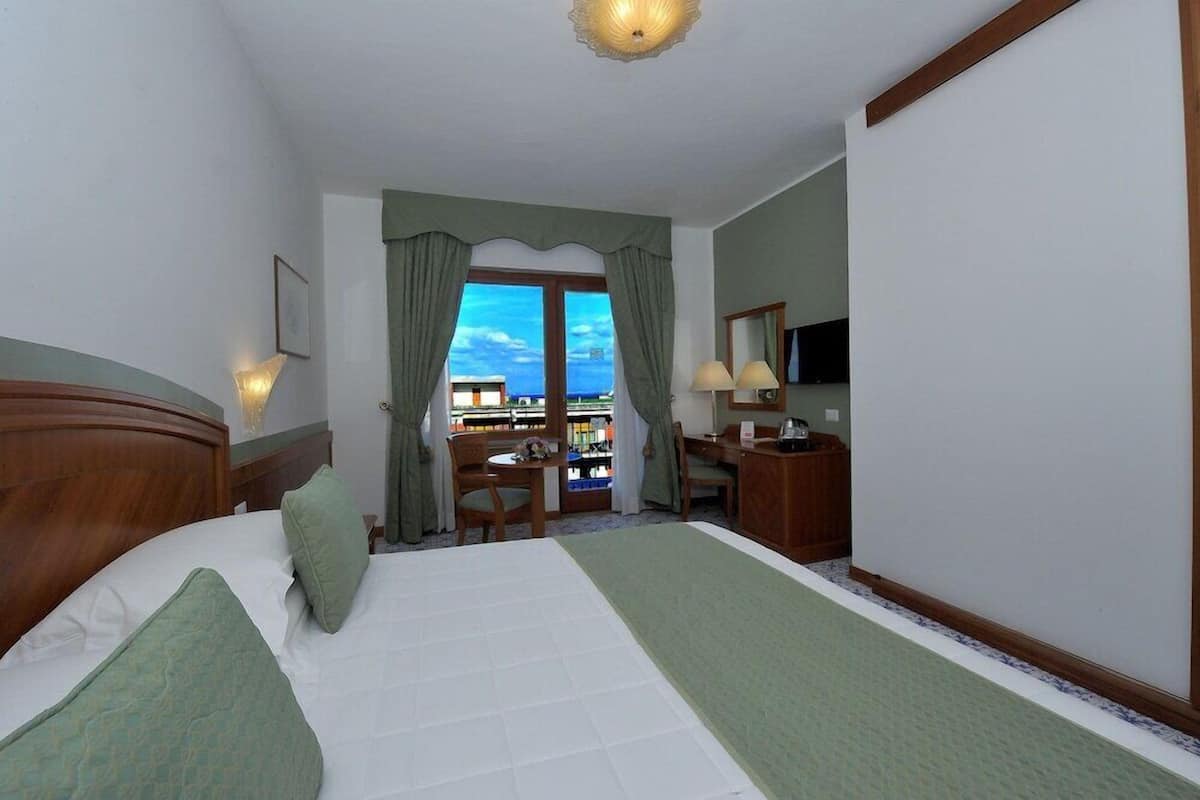 Ein Hotelzimmer mit Bett, Schreibtisch, Stuhl, Fernseher und einem Balkon mit Blick.