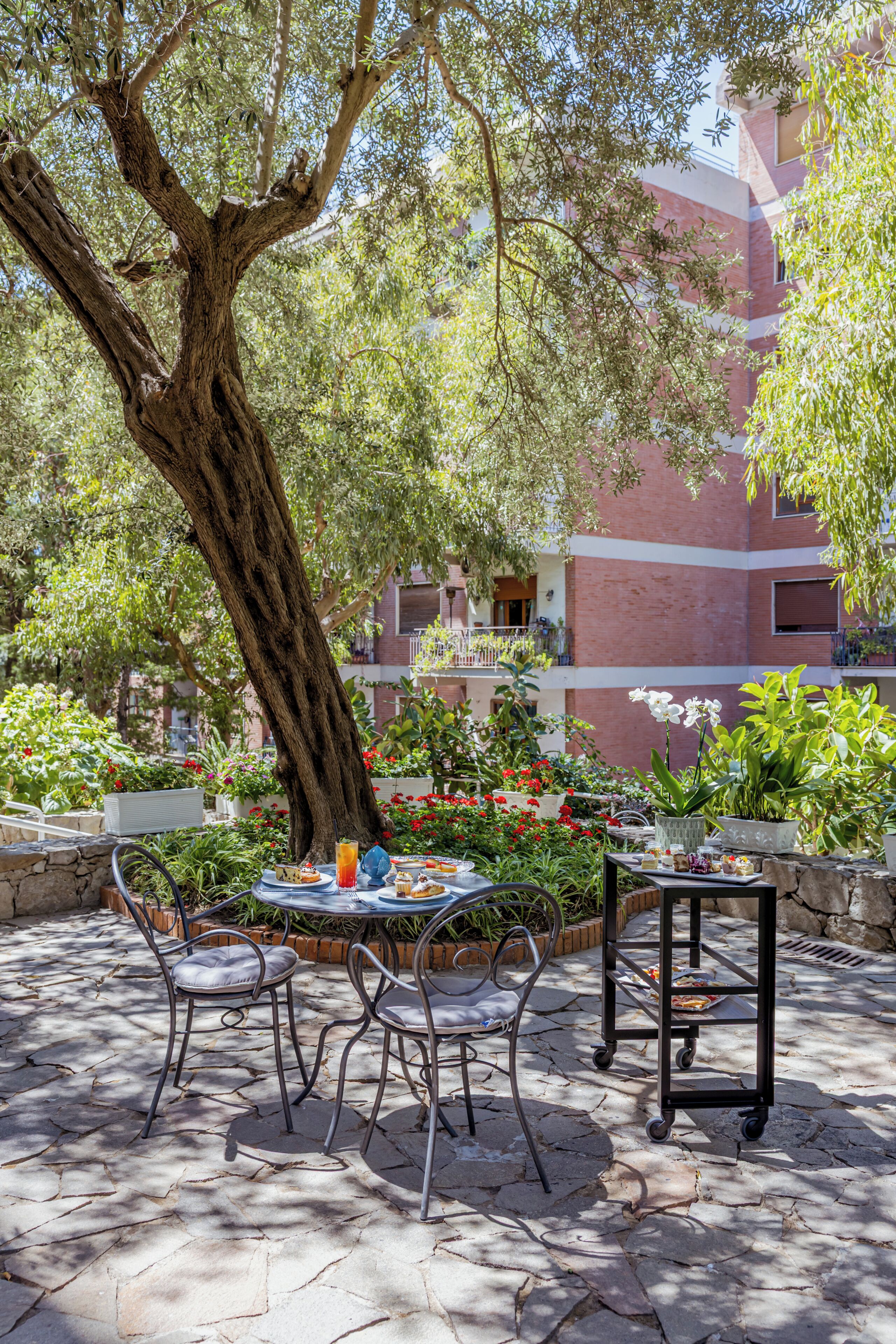 Un patio al aire libre con una mesa y sillas, rodeado de plantas y un árbol grande.