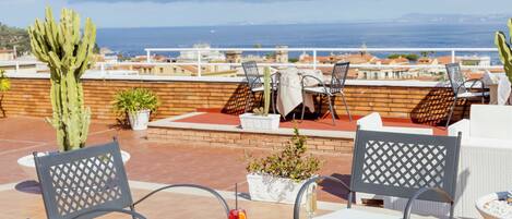 Una terraza con asientos exteriores, un cactus y vista al mar.