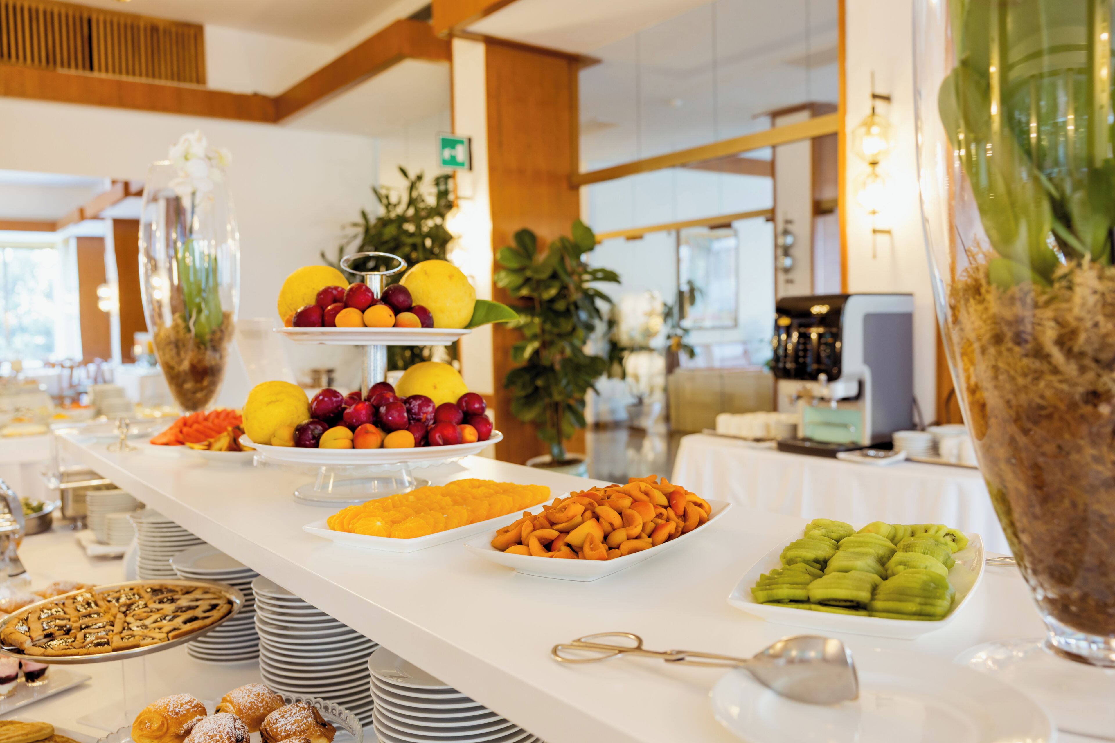 A buffet with various food items, including fruits, pastries, and a large decorative vase.
