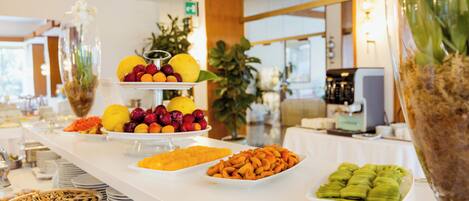 A buffet with various food items, including fruits, pastries, and a large decorative vase.