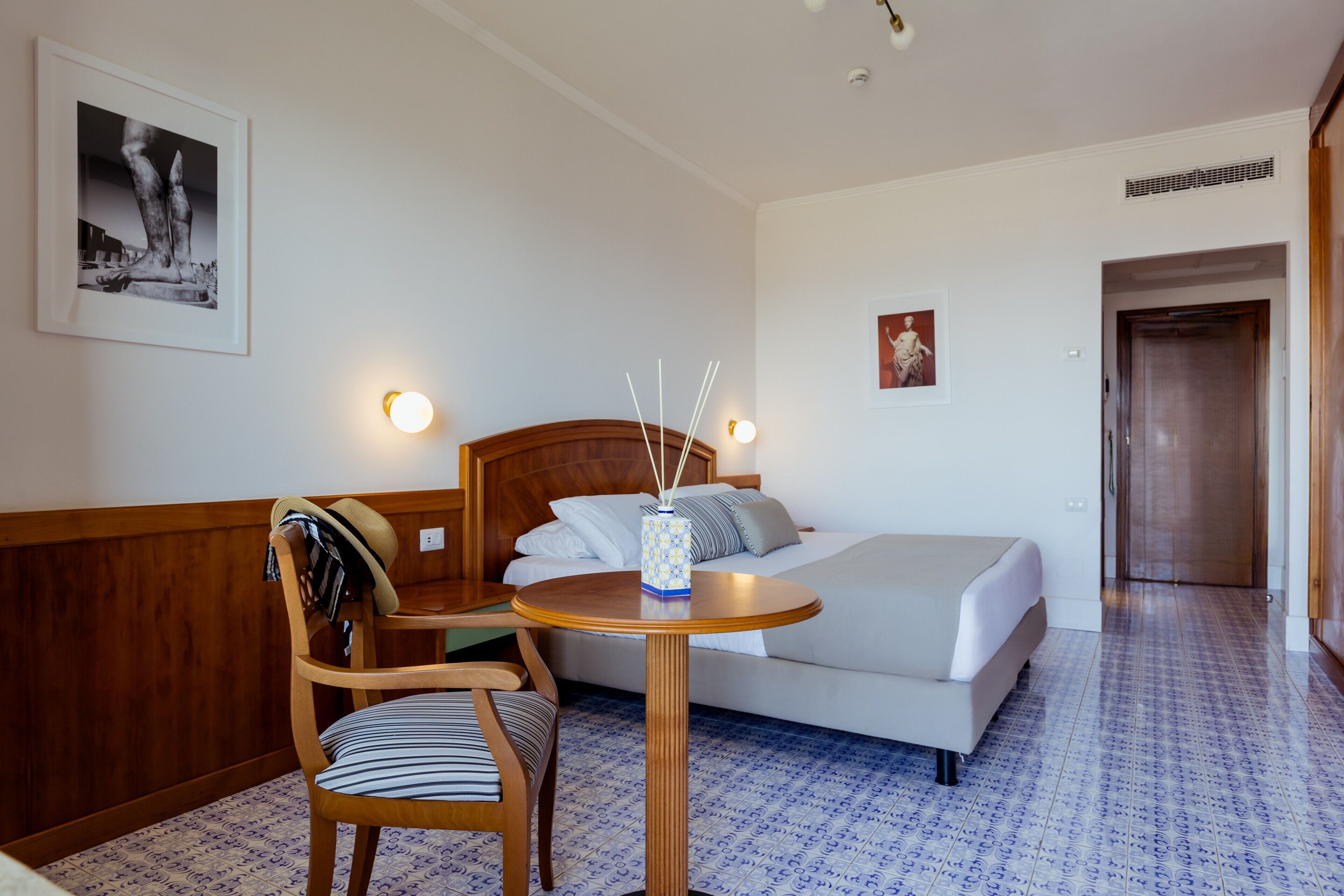 Habitación de hotel con cama, una mesa redonda de madera, una silla, un cuadro en la pared y una puerta.