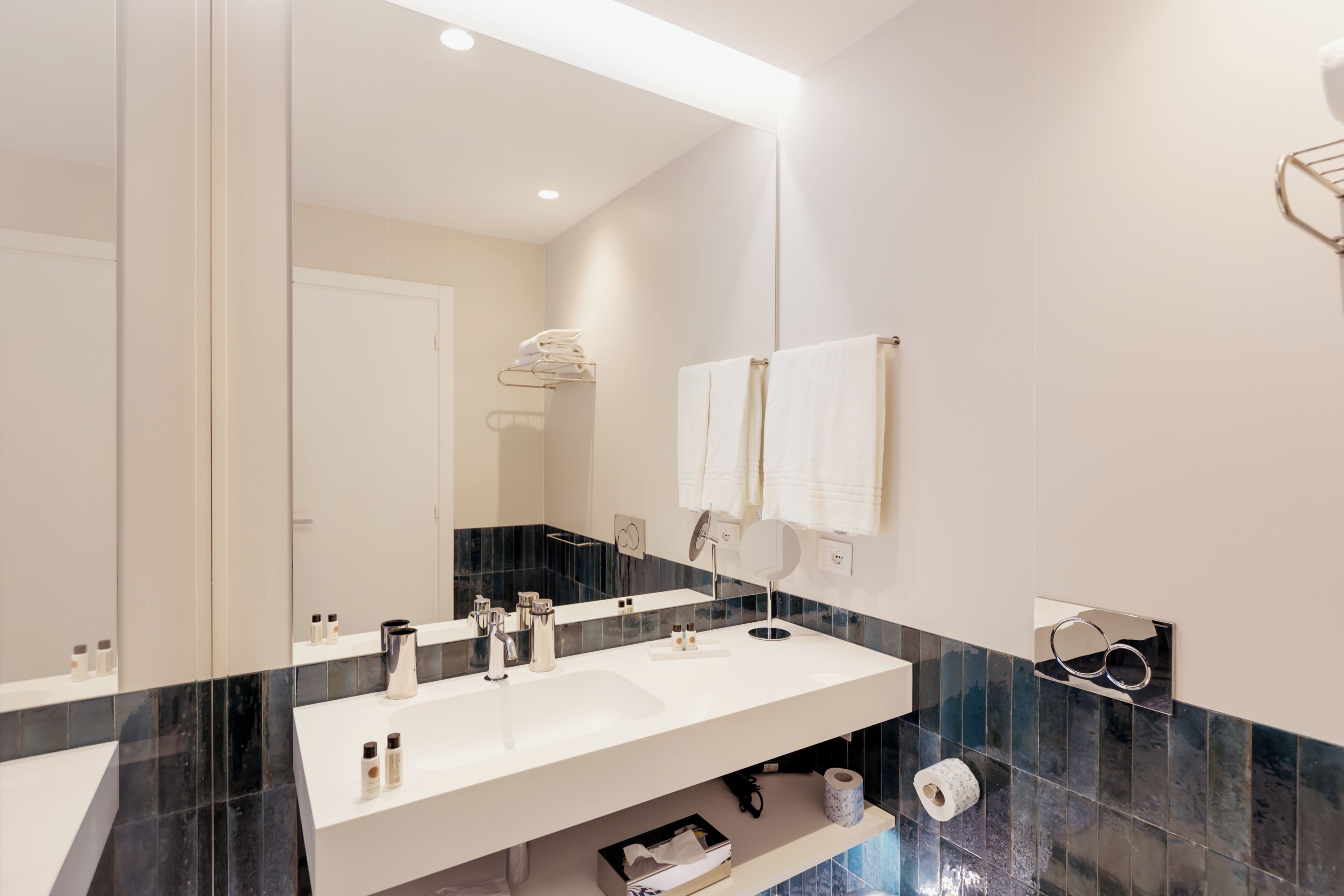 Een moderne badkamer met een grote spiegel, twee wastafels en een verzorgingshoek.
