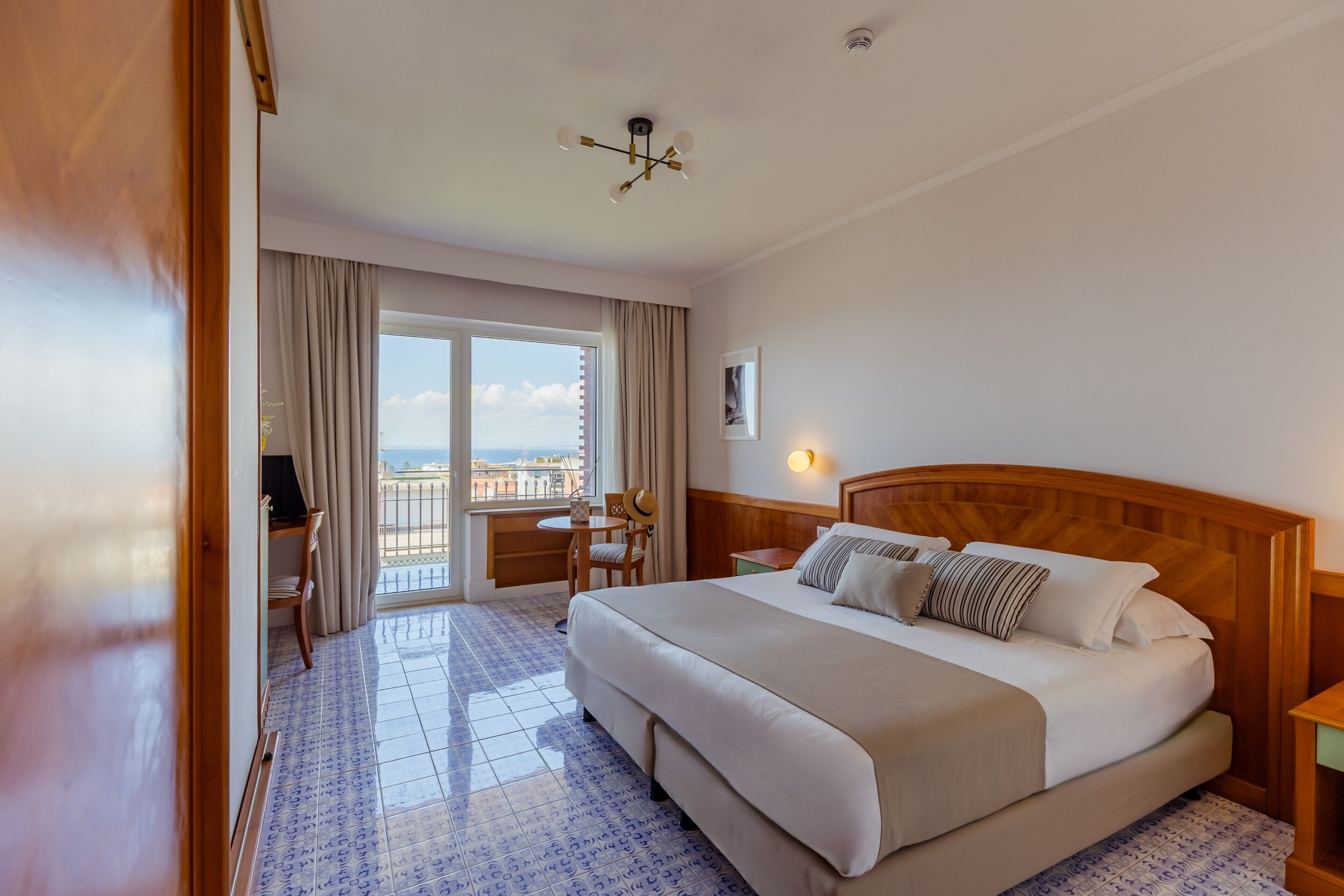 Habitación de hotel con cama, escritorio, silla, ventana con cortinas y vista a la ciudad.
