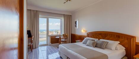 Habitación de hotel con cama, escritorio, silla, ventana con cortinas y vista a la ciudad.