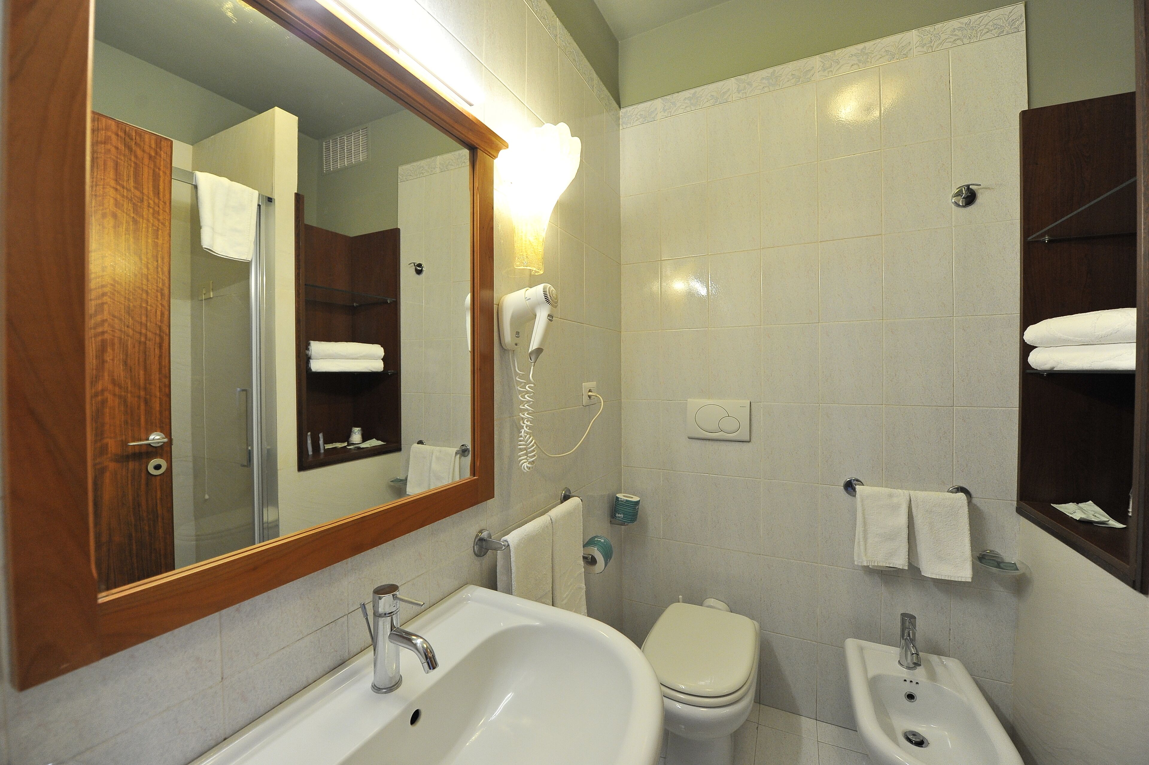 A bathroom with a sink, toilet, bidet, and a mirror with a light.